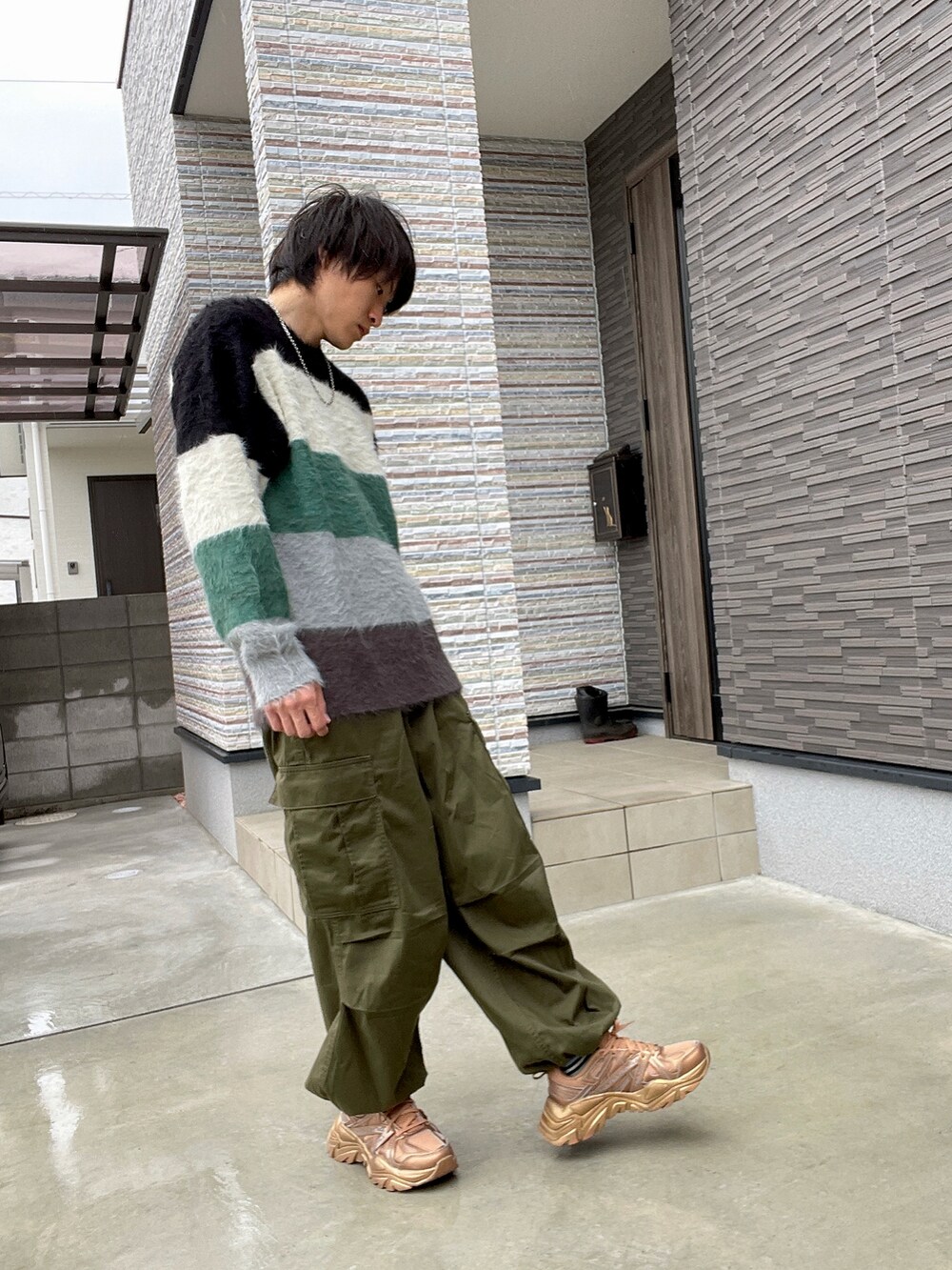 ブラック系のニット/セーター、グリーン系のカーゴパンツ、ゴールド系のスニーカーを着用したメンズの春コーディネートの2枚目の写真