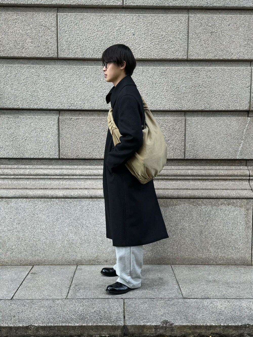 ブラック系のステンカラーコート、グレー系のスウェットパンツ、ブラック系のドレスシューズを着用したメンズの冬コーディネートの2枚目の写真