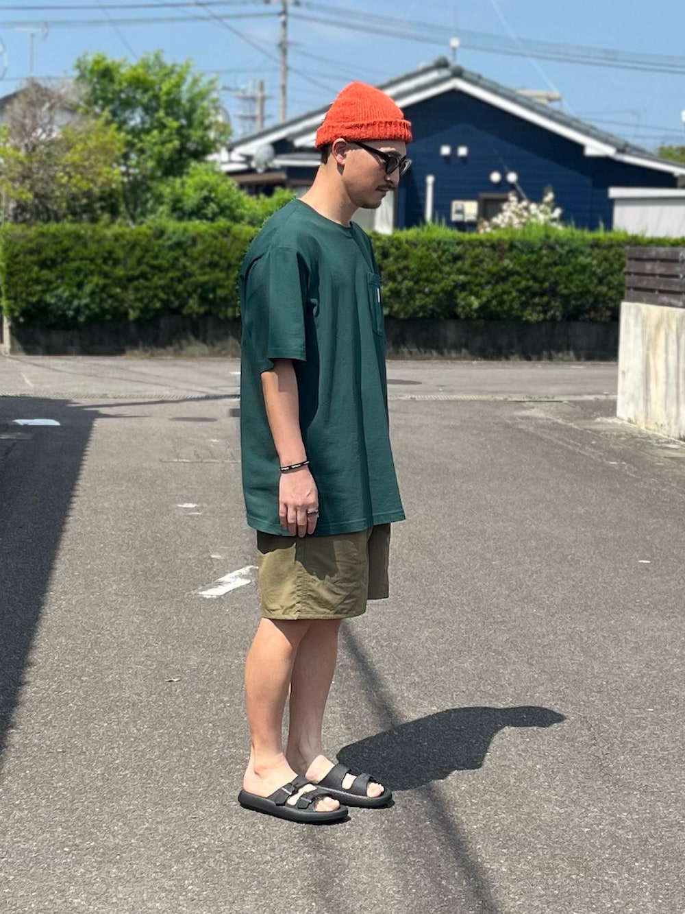 グリーン系のTシャツ/カットソー、ブラウン系のパンツ、ブラック系のサンダルを着用したメンズの春コーディネートの2枚目の写真