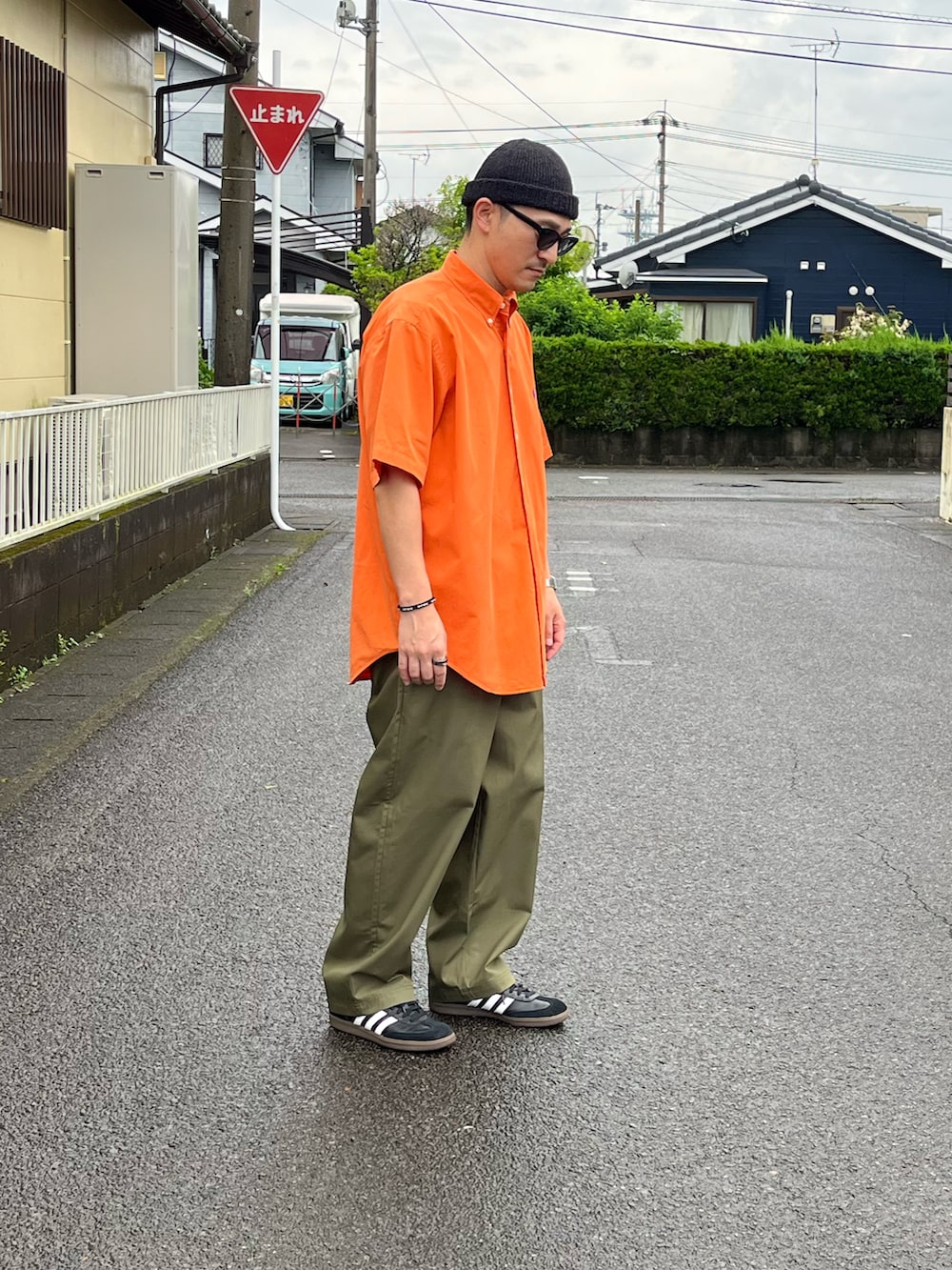 オレンジ系のシャツ/ブラウス、グリーン系のチノパンツ、ブラック系のスニーカーを着用したメンズの春コーディネートの2枚目の写真