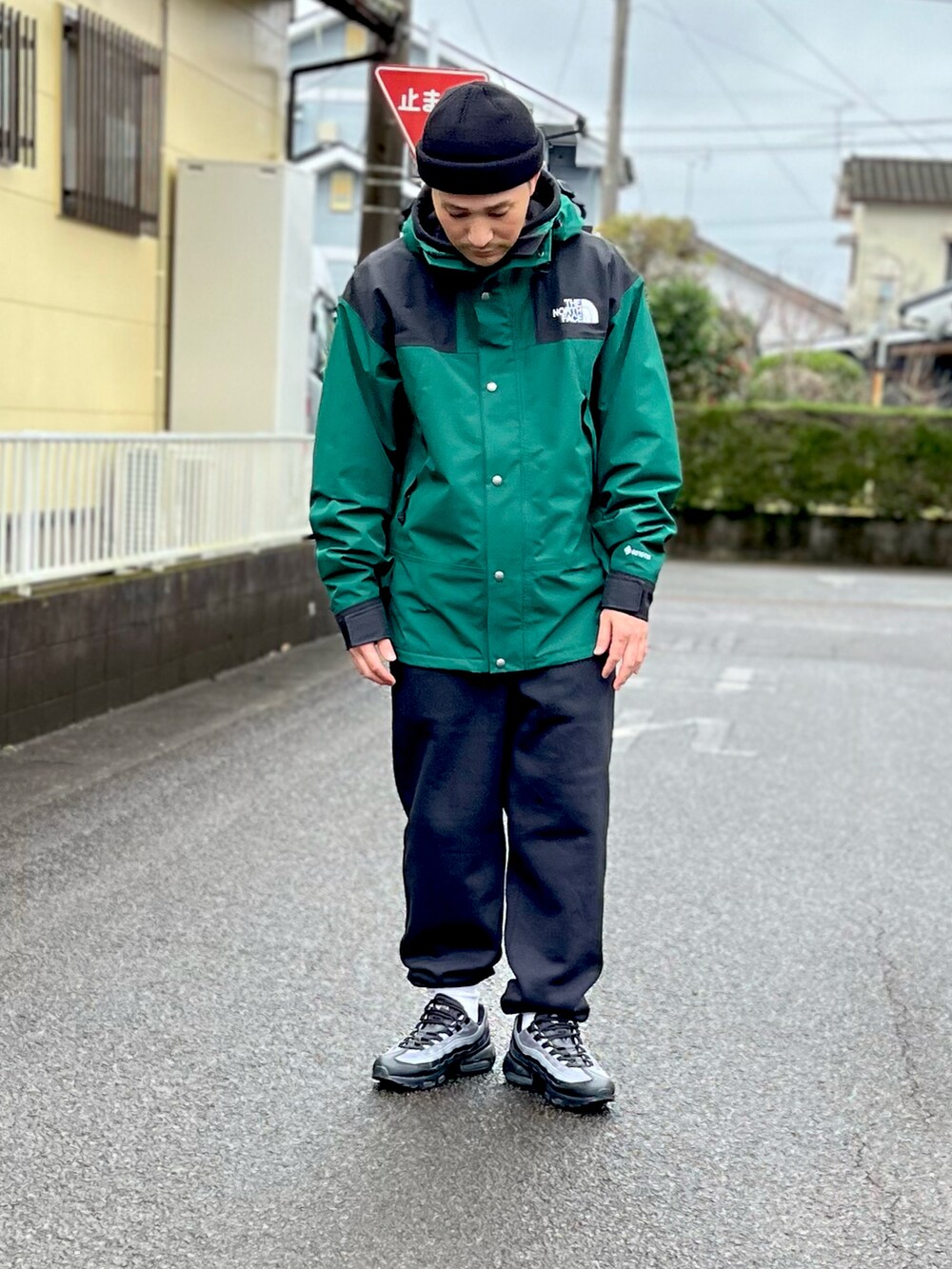 グリーン系のマウンテンパーカー、ブラック系のスウェットパンツ、ブラック系のスニーカーを着用したメンズの冬コーディネートの2枚目の写真