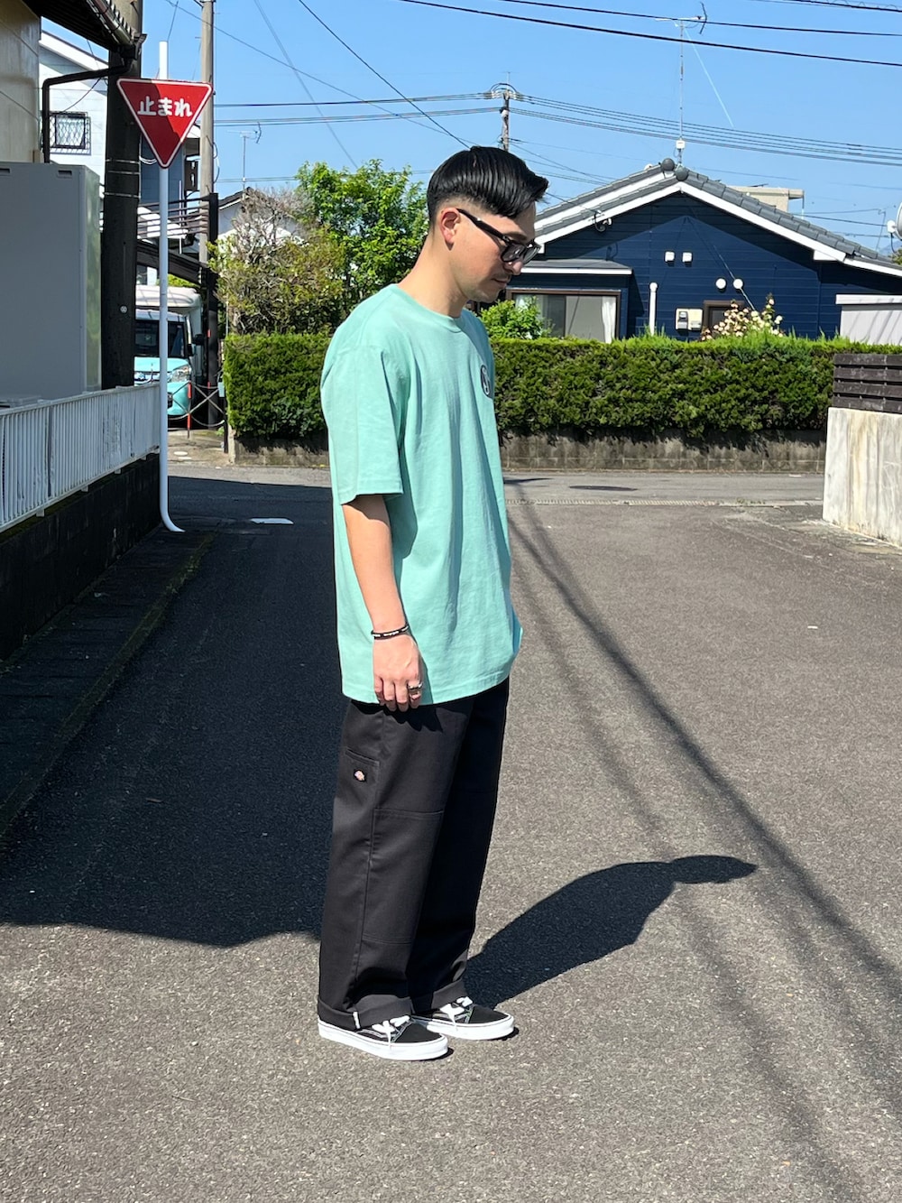 グリーン系のTシャツ/カットソー、グレー系のチノパンツ、ブラック系のスニーカーを着用したメンズの春コーディネートの3枚目の写真