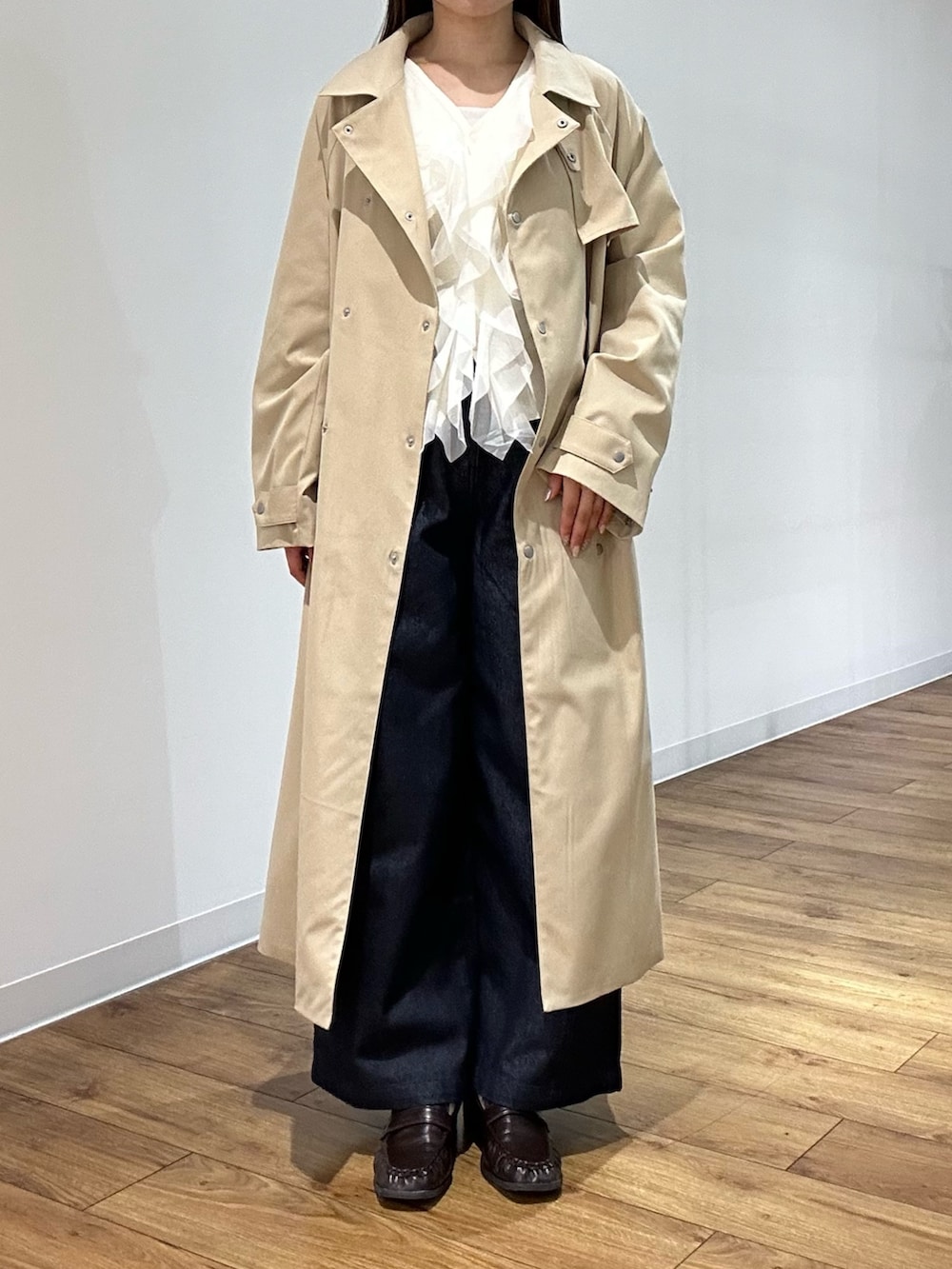 ベージュ系のトレンチコート、ホワイト系のカーディガン/ボレロ、ブルー系のデニムパンツを着用したレディースの春コーディネートの3枚目の写真