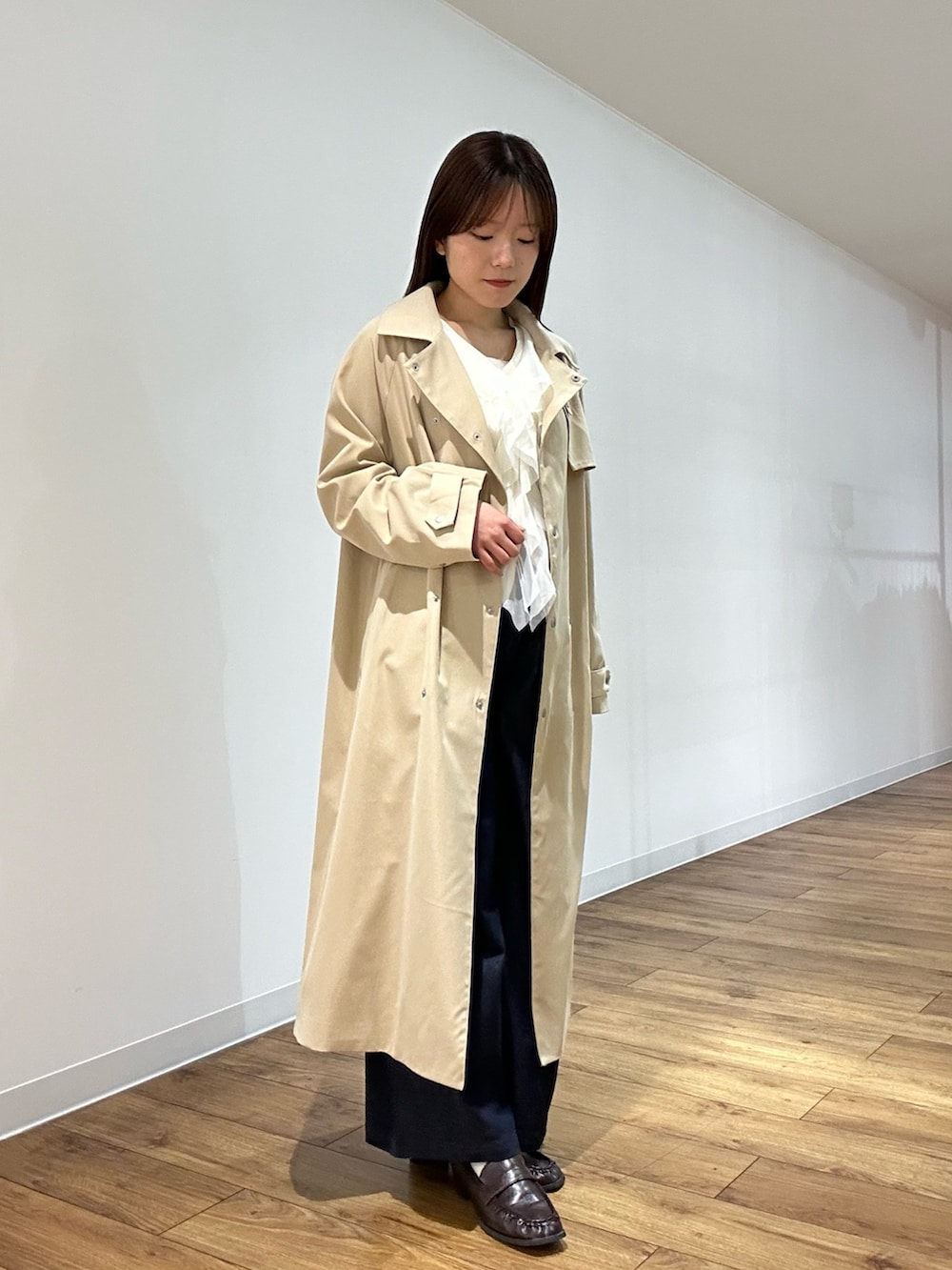 ベージュ系のトレンチコート、ホワイト系のカーディガン/ボレロ、ブルー系のデニムパンツを着用したレディースの春コーディネートの2枚目の写真