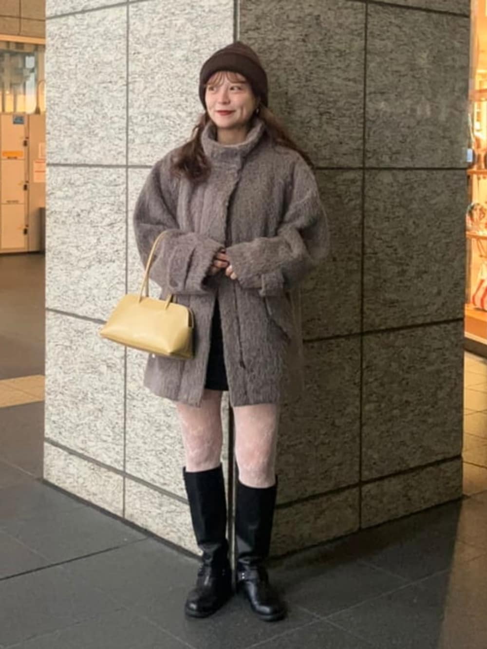 イエロー系のトートバッグ、ブラウン系のステンカラーコート、ブラウン系のニットキャップ/ビーニーを着用したレディースの秋コーディネートの2枚目の写真