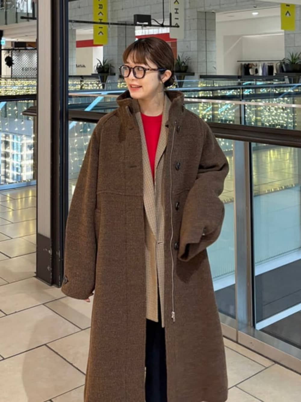 ブラウン系のステンカラーコート、ブラウン系のテーラードジャケット、レッド系のニット/セーターを着用したレディースの冬コーディネートの2枚目の写真