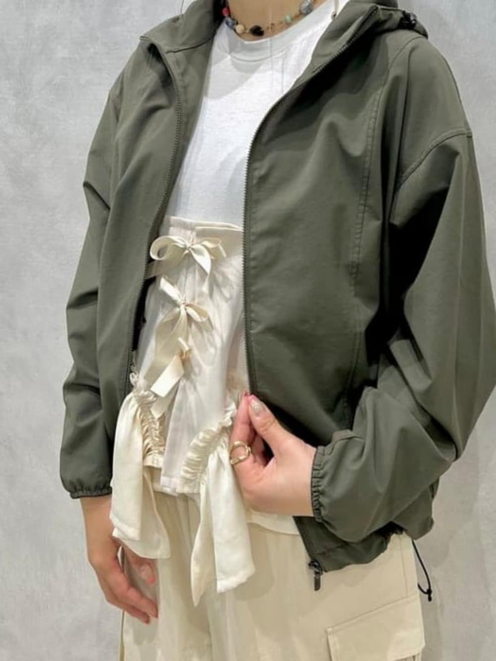 グリーン系のナイロンジャケット、ブラック系のドレスシューズ、ホワイト系のカーゴパンツを着用したレディースの夏コーディネートの2枚目の写真