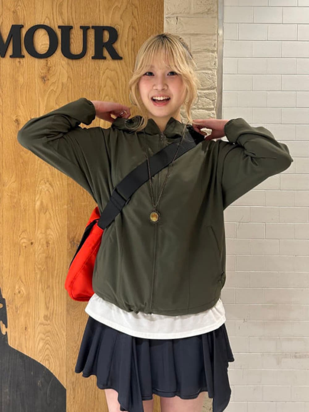 グリーン系のナイロンジャケット、グレー系のスカート、レッド系のメッセンジャーバッグを着用したレディースの春コーディネートの2枚目の写真