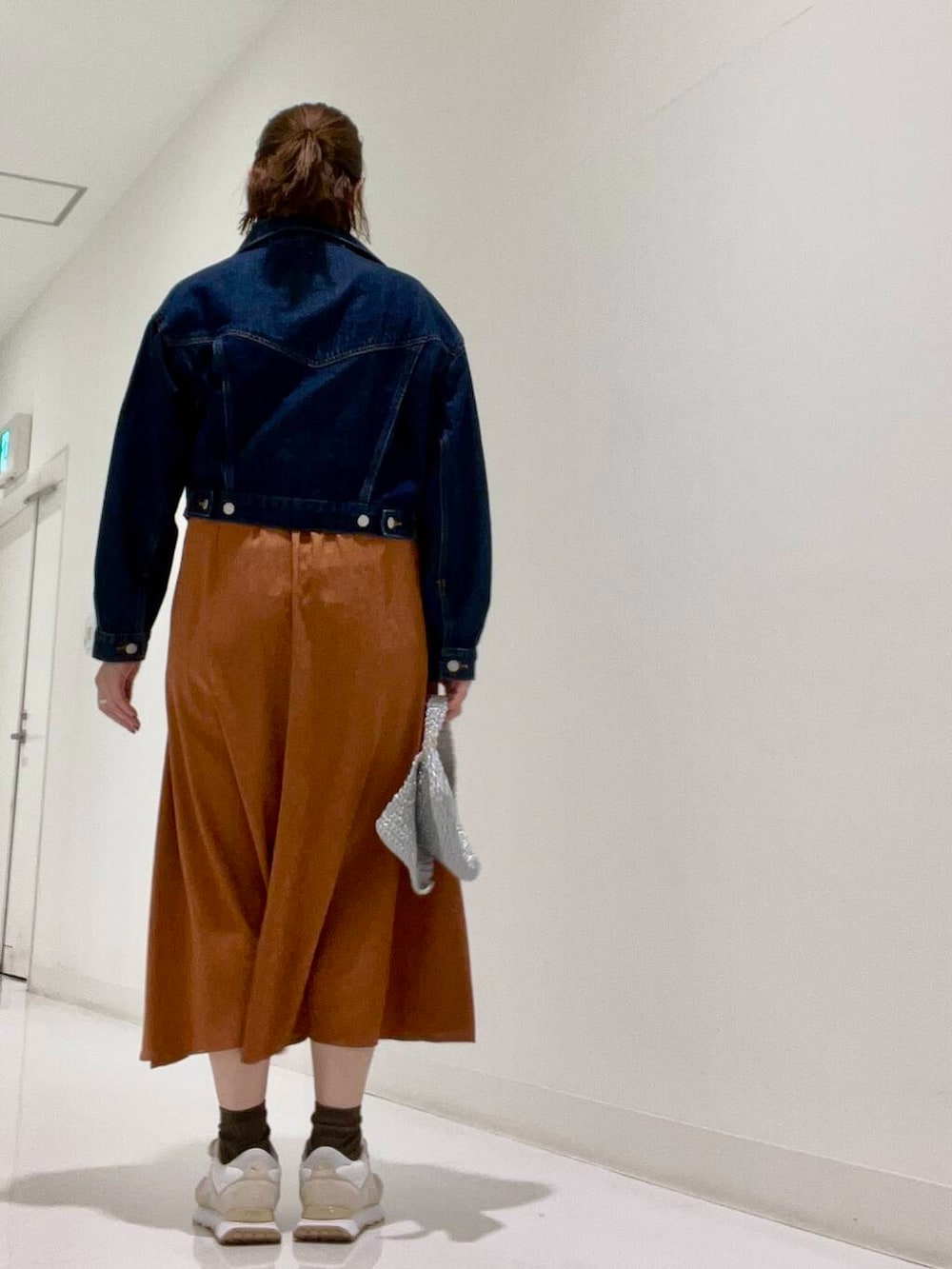 シルバー系のハンドバッグ、ブルー系のデニムジャケット、ホワイト系のスニーカーを着用したレディースの夏コーディネートの3枚目の写真