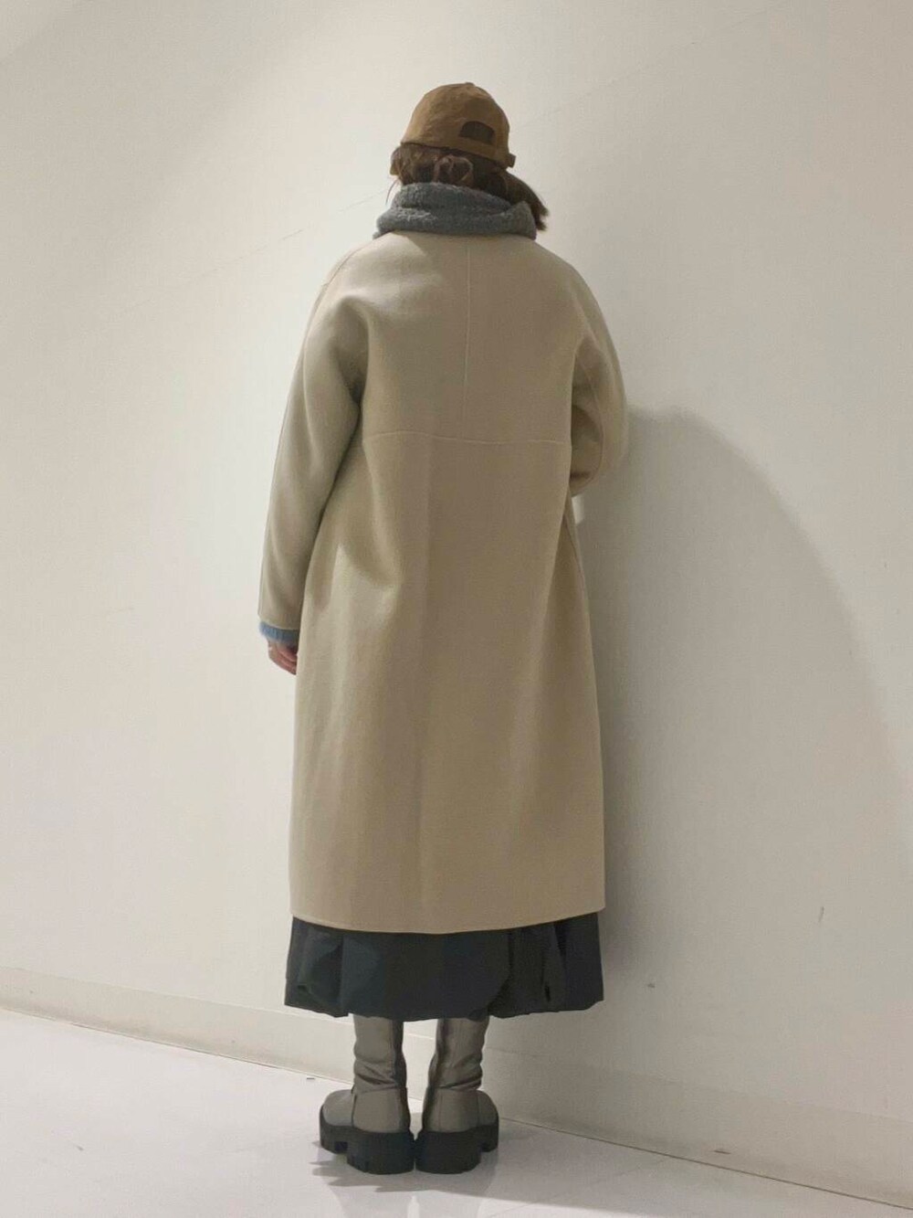 ベージュ系のステンカラーコート、シルバー系のブーツ、グレー系のワンピースを着用したレディースの冬コーディネートの3枚目の写真