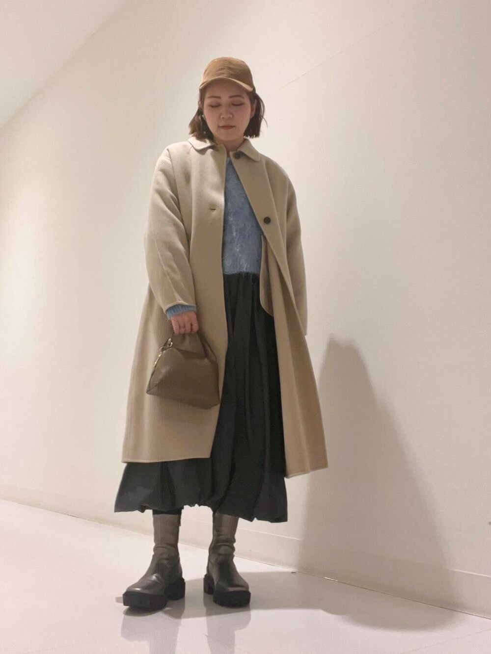 ベージュ系のステンカラーコート、シルバー系のブーツ、グレー系のワンピースを着用したレディースの冬コーディネートの6枚目の写真