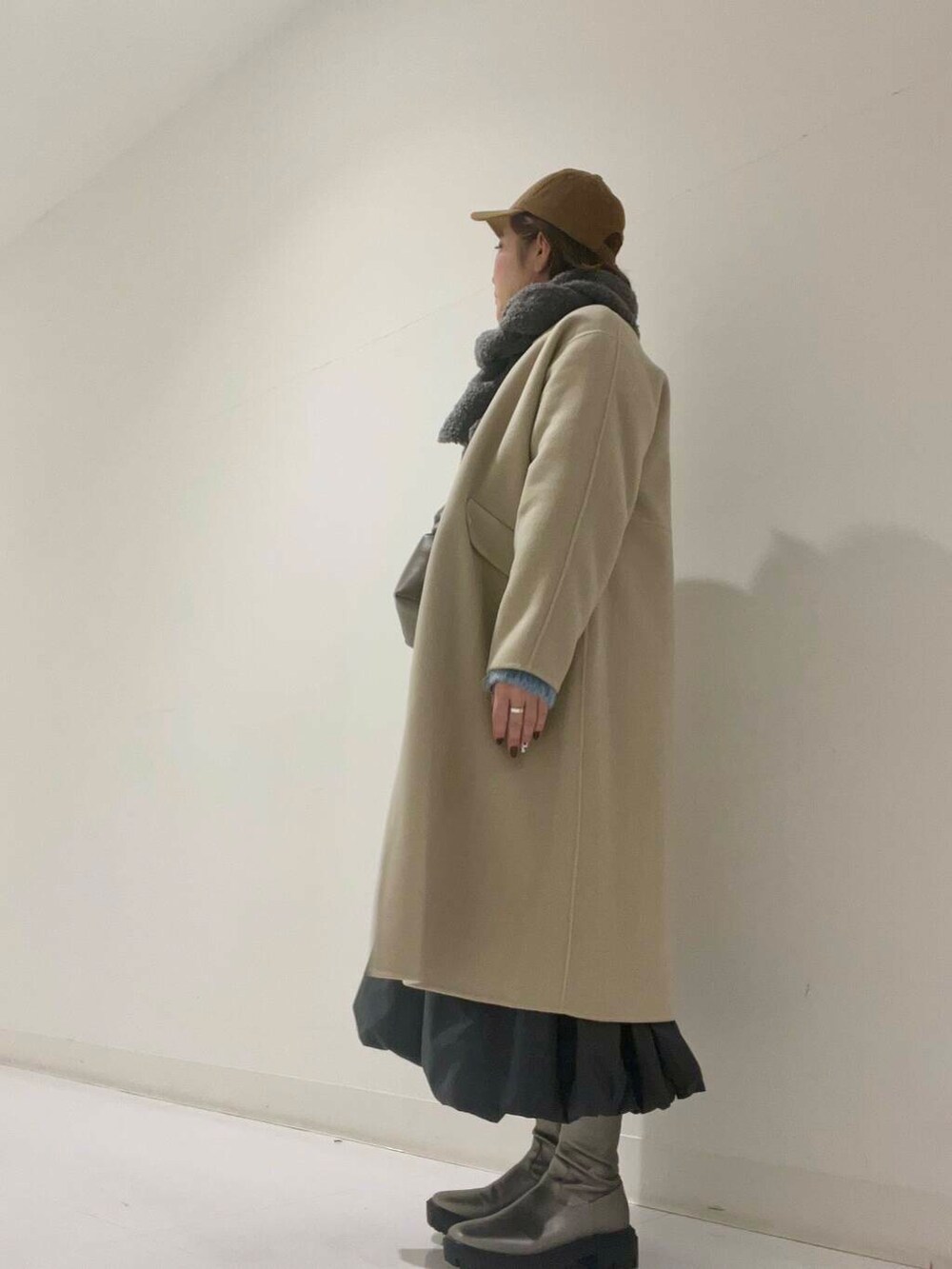 ベージュ系のステンカラーコート、シルバー系のブーツ、グレー系のワンピースを着用したレディースの冬コーディネートの2枚目の写真