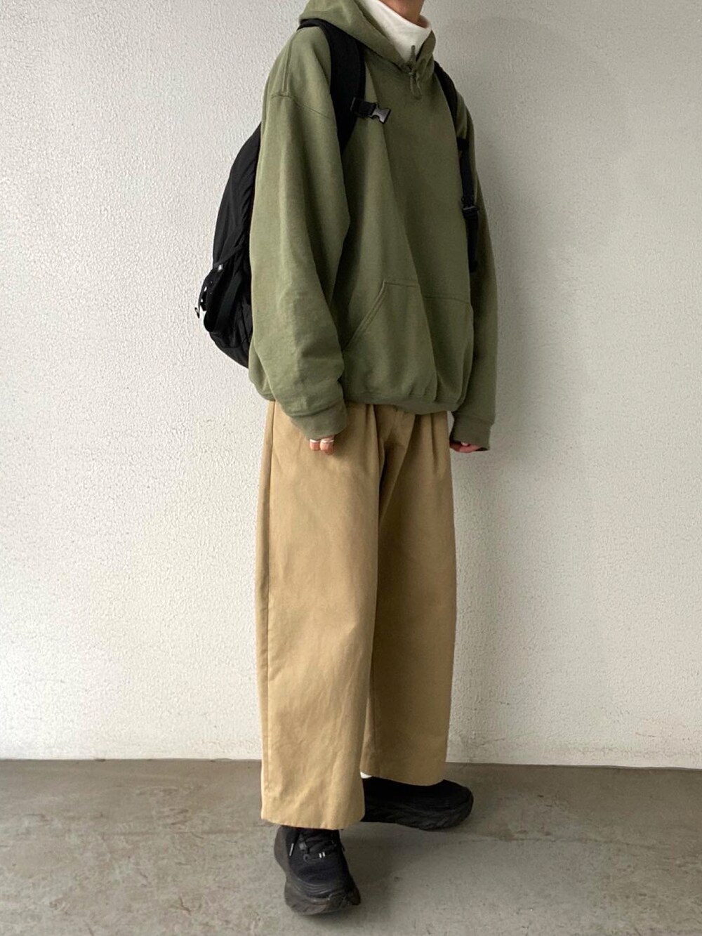 グリーン系のパーカー、ベージュ系のチノパンツ、ブラック系のスニーカーを着用したメンズの秋コーディネートの3枚目の写真