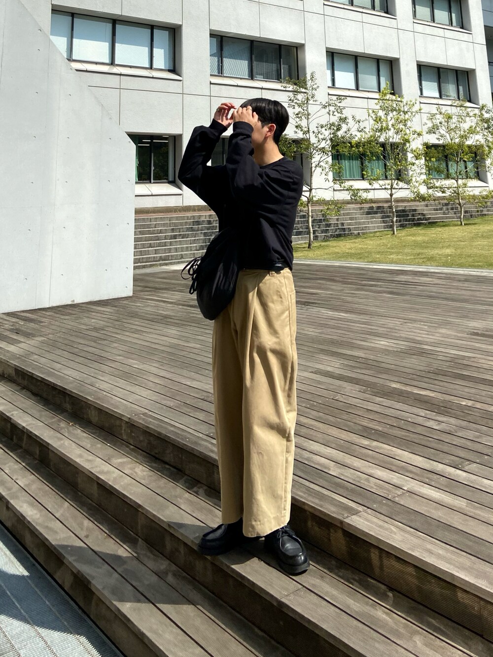 ブラック系のTシャツ/カットソー、ブラック系のショルダーバッグ、ベージュ系のチノパンツを着用したメンズの春コーディネートの2枚目の写真