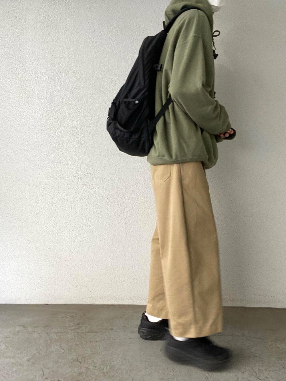 グリーン系のパーカー、ベージュ系のチノパンツ、ブラック系のスニーカーを着用したメンズの秋コーディネートの2枚目の写真