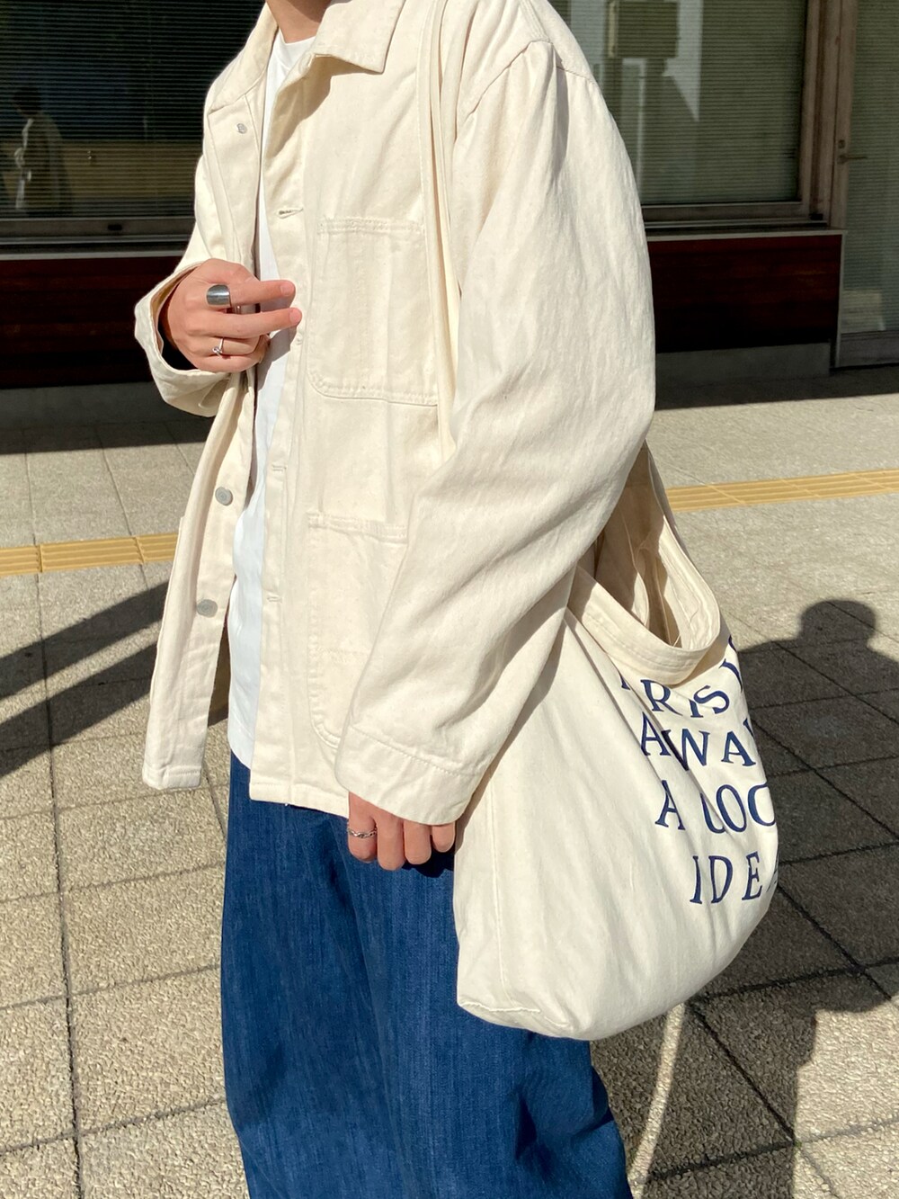 ホワイト系のカバーオール、ベージュ系のショルダーバッグ、ブルー系のデニムパンツを着用したメンズの春コーディネートの3枚目の写真