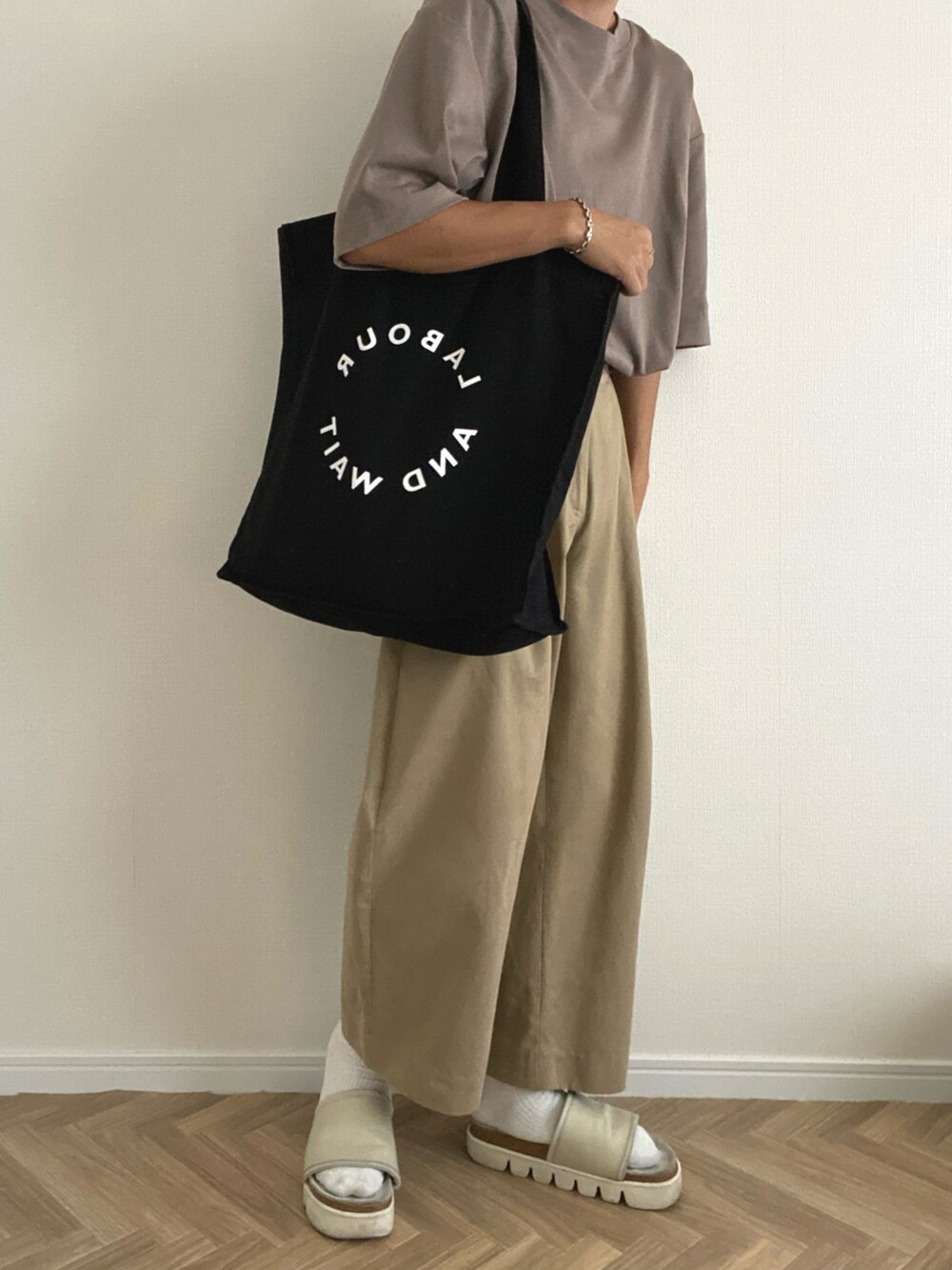 ブラウン系のTシャツ/カットソー、ブラック系のトートバッグ、ホワイト系のサンダルを着用したメンズの夏コーディネートの2枚目の写真