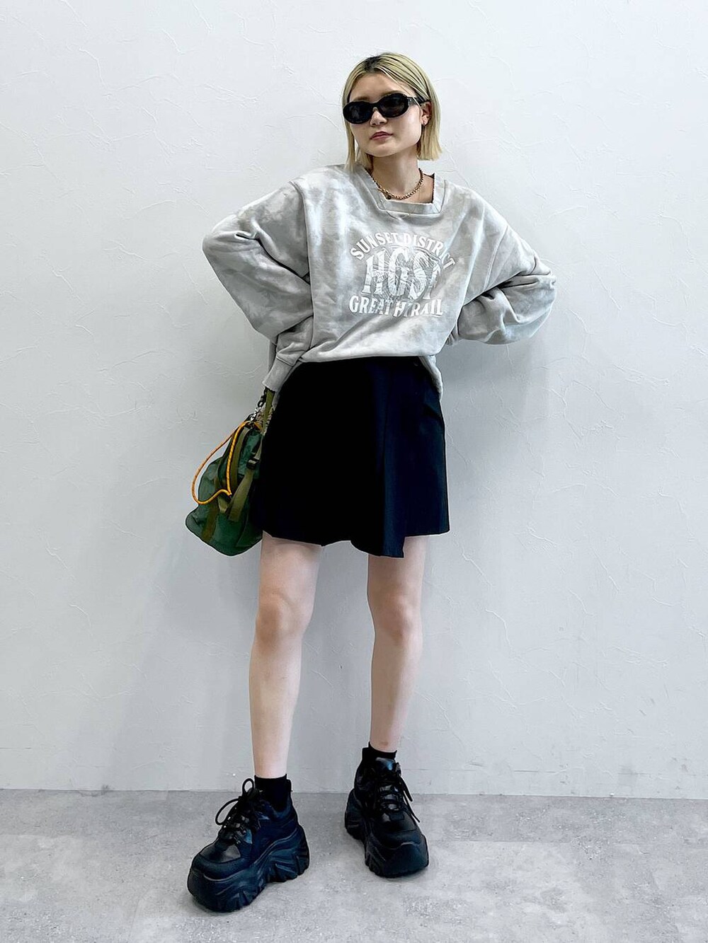 ブラック系のブーツ、ブラック系のスカート、グリーン系のショルダーバッグを着用したレディースの秋コーディネートの2枚目の写真