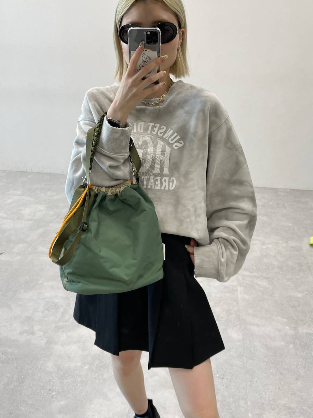 ブラック系のブーツ、ブラック系のスカート、グリーン系のショルダーバッグを着用したレディースの秋コーディネートの4枚目の写真