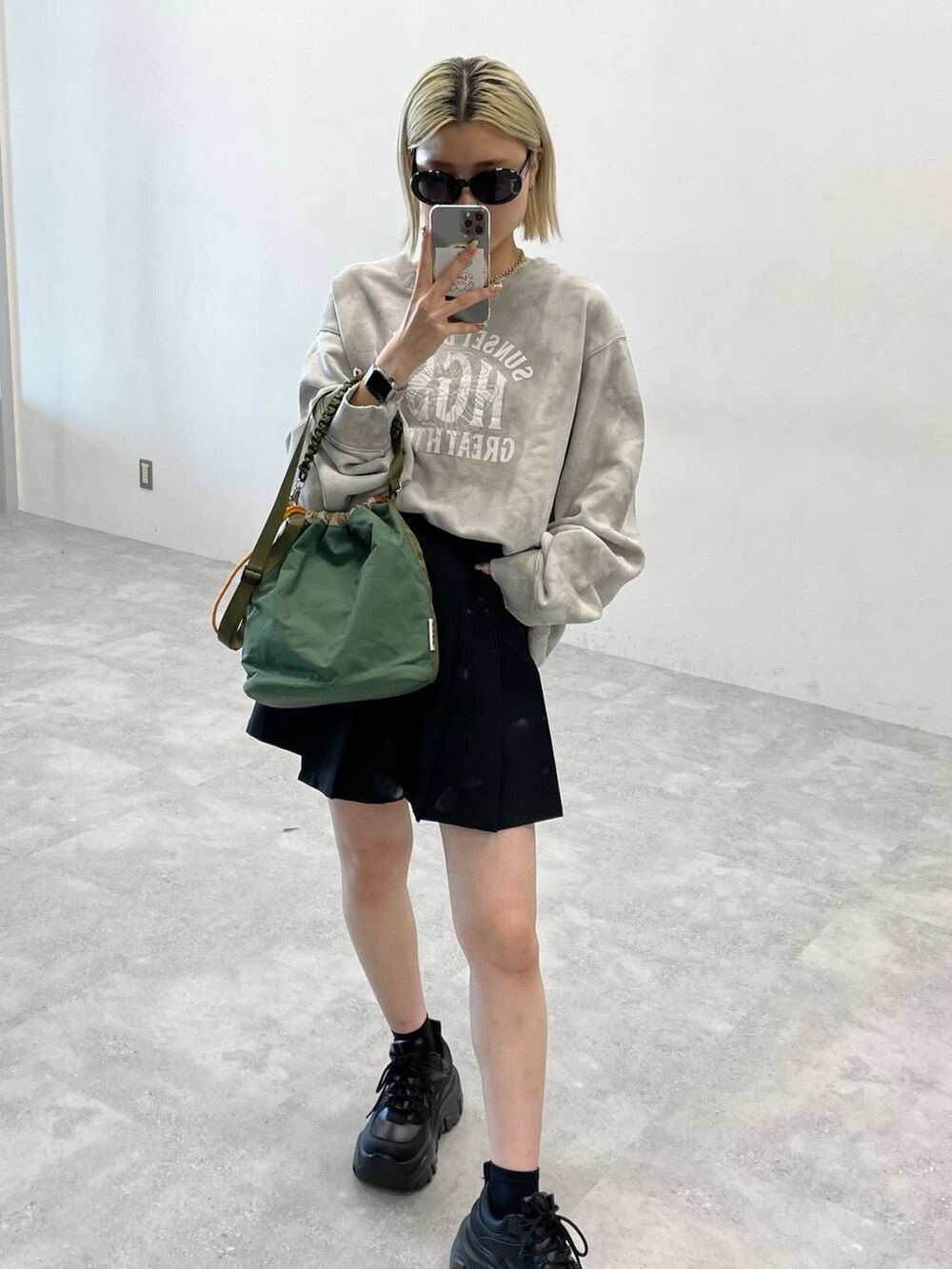 ブラック系のブーツ、ブラック系のスカート、グリーン系のショルダーバッグを着用したレディースの秋コーディネートの3枚目の写真