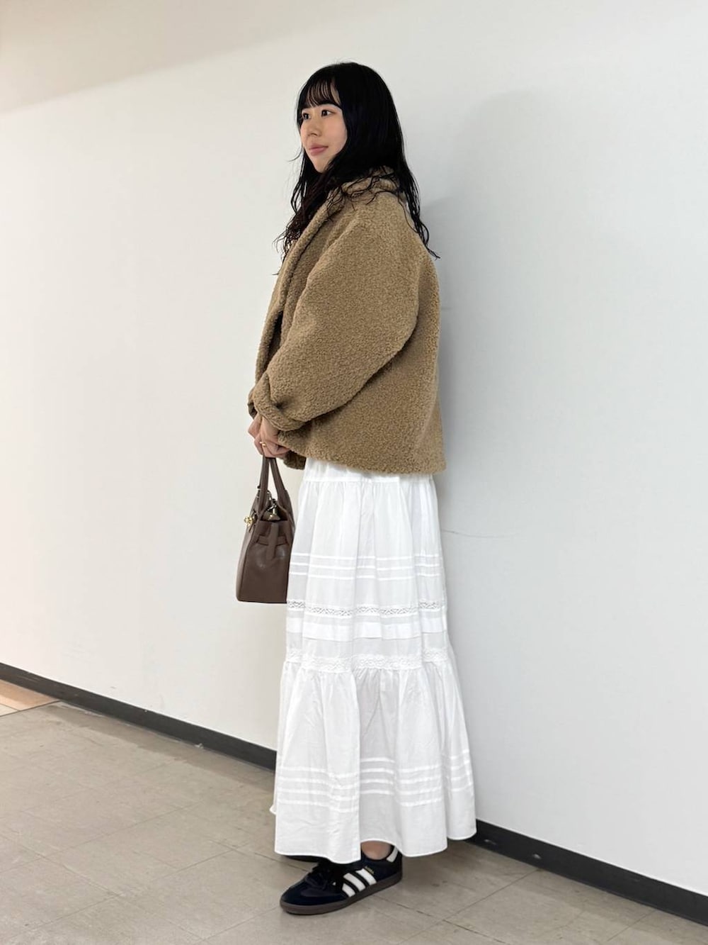イエロー系のピーコート、ベージュ系のショルダーバッグ、ホワイト系のスカートを着用したレディースの秋コーディネートの2枚目の写真