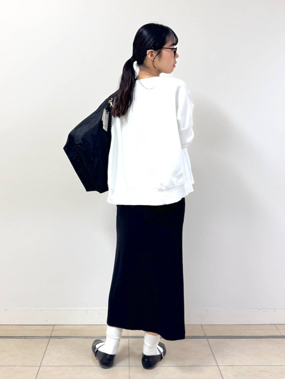 ブラック系のショルダーバッグ、ホワイト系のニット/セーター、ブラック系のスカートを着用したレディースの冬コーディネートの2枚目の写真