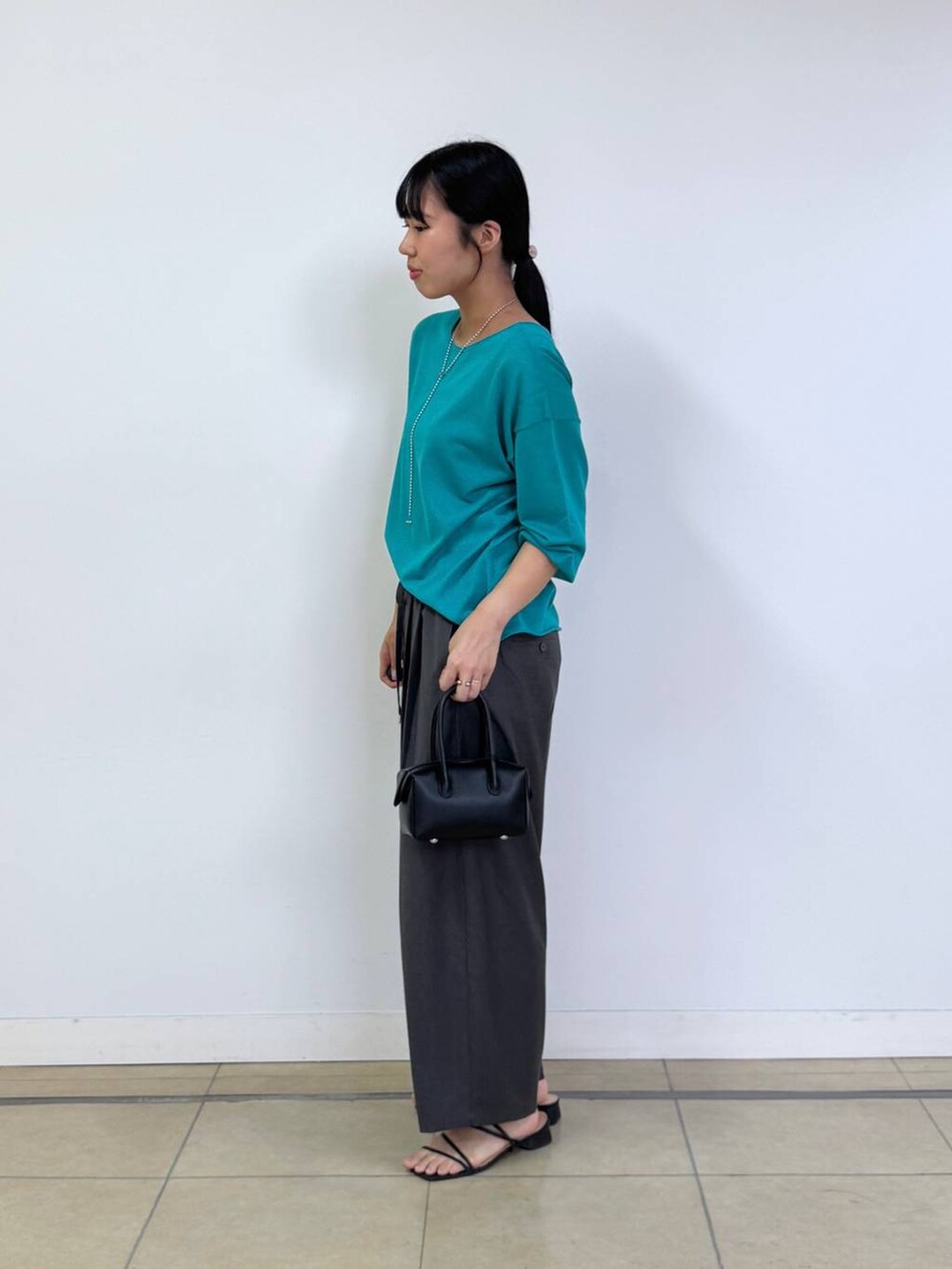 ブラック系のハンドバッグ、グリーン系のニット/セーター、グレー系のその他パンツを着用したレディースの夏コーディネートの2枚目の写真