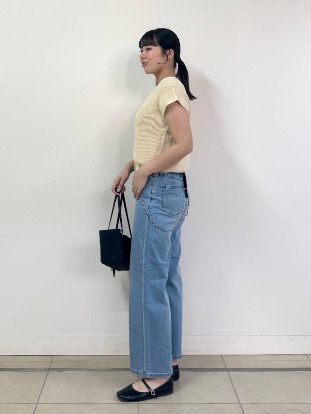 ブルー系のデニムパンツ、ホワイト系のベスト、ブラック系のかごバッグを着用したレディースの春コーディネートの2枚目の写真