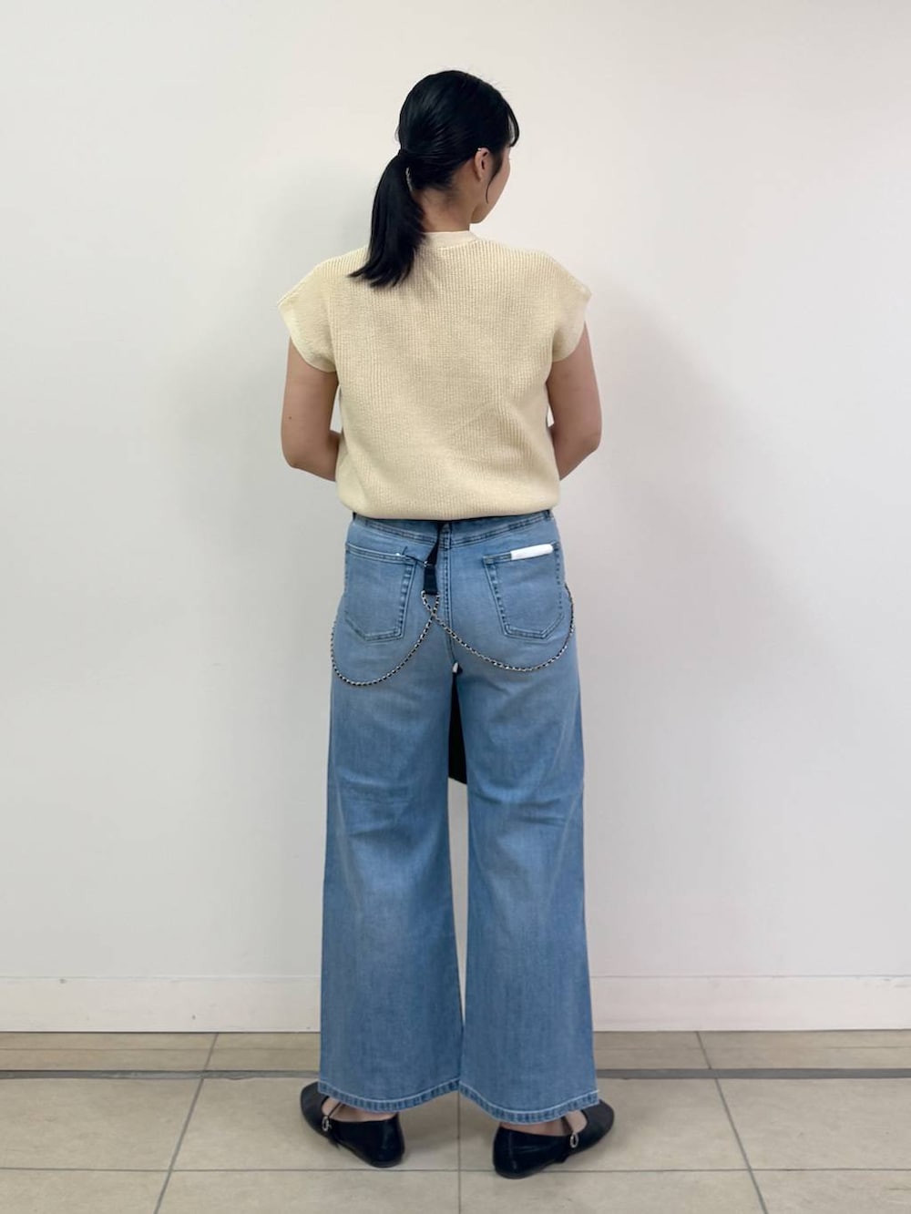 ブルー系のデニムパンツ、ホワイト系のベスト、ブラック系のかごバッグを着用したレディースの春コーディネートの3枚目の写真