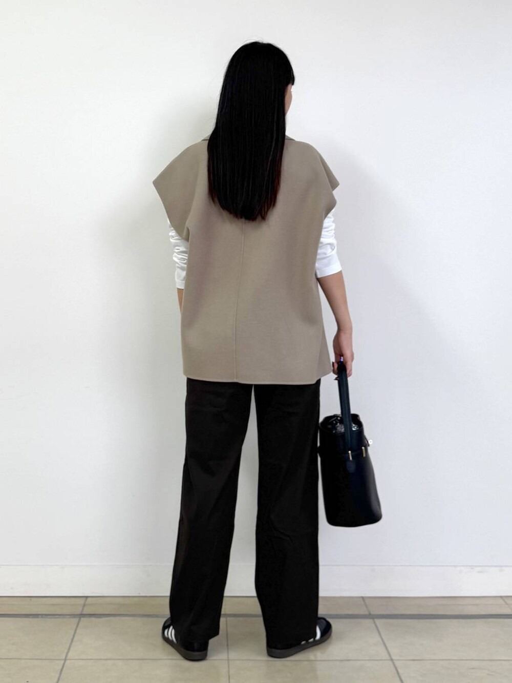 ブラウン系のチノパンツ、ベージュ系のベスト、ブラック系のハンドバッグを着用したレディースの秋コーディネートの3枚目の写真