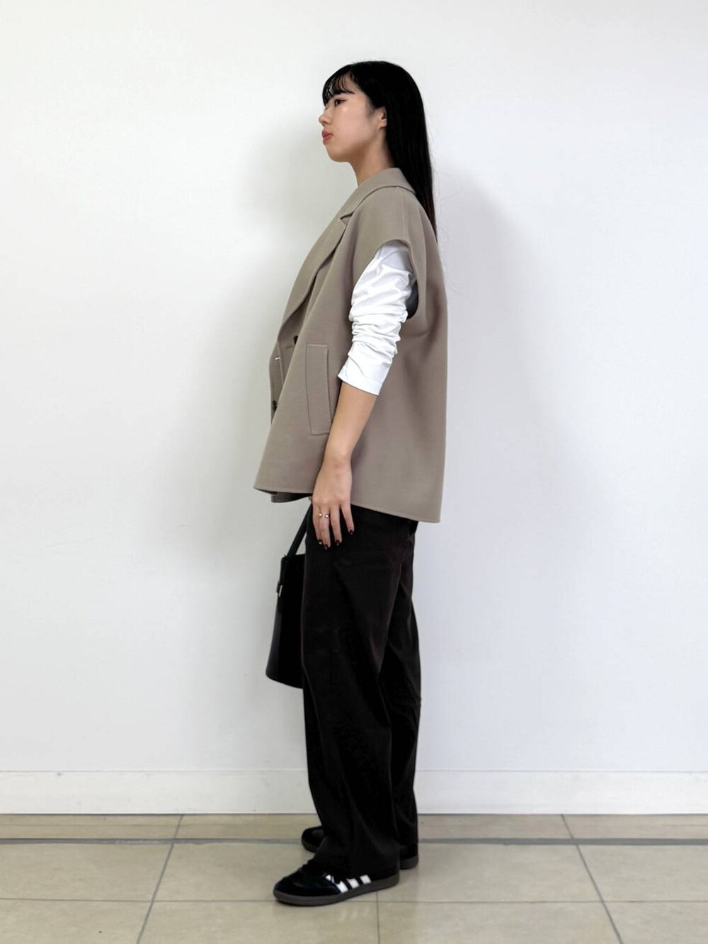 ブラウン系のチノパンツ、ベージュ系のベスト、ブラック系のハンドバッグを着用したレディースの秋コーディネートの2枚目の写真