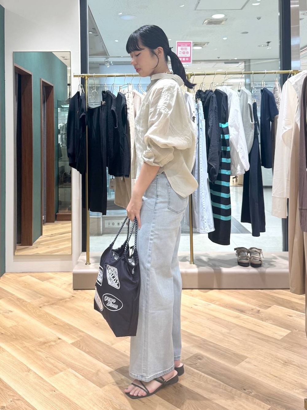 ブルー系のデニムパンツ、ブルー系のトートバッグ、ベージュ系のシャツ/ブラウスを着用したレディースの夏コーディネートの2枚目の写真