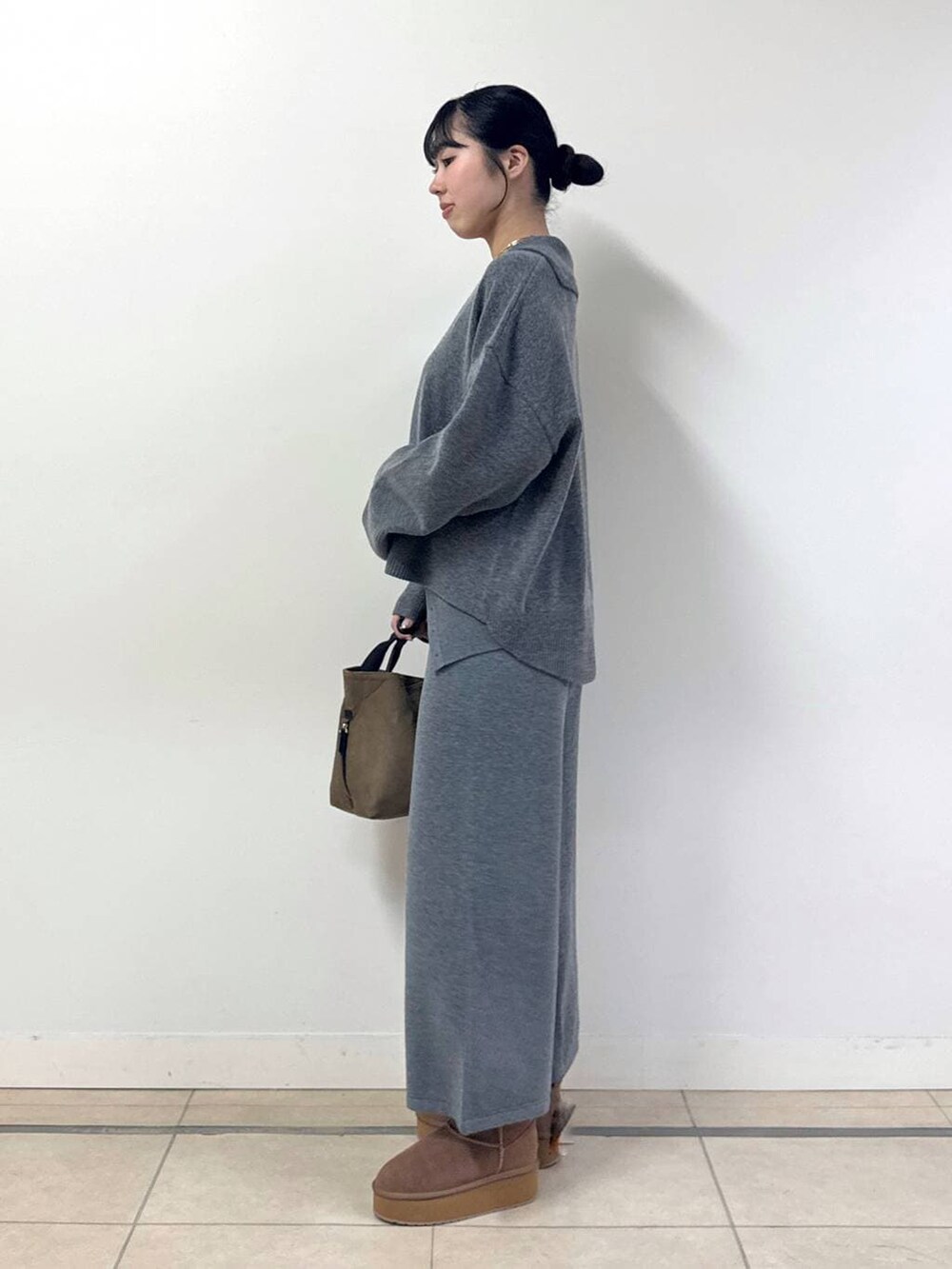 イエロー系のトートバッグ、イエロー系のブーツ、グレー系のニット/セーターを着用したレディースの冬コーディネートの2枚目の写真