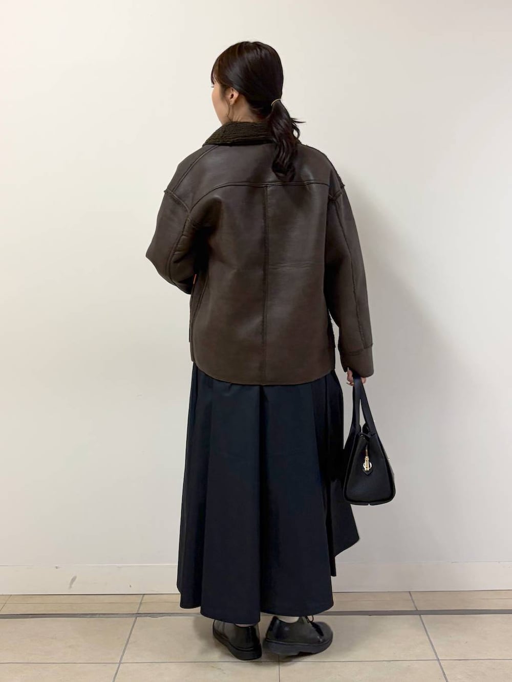 ブラウン系のムートンコート、ホワイト系のTシャツ/カットソー、ブラック系のハンドバッグを着用したレディースの秋コーディネートの3枚目の写真