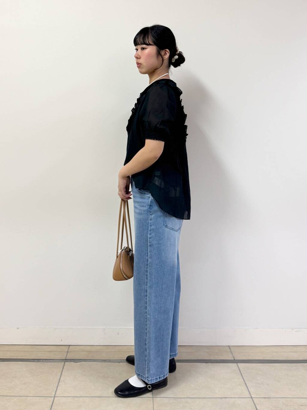 ブルー系のデニムパンツ、ブラック系のシャツ/ブラウス、ブラウン系のハンドバッグを着用したレディースの春コーディネートの2枚目の写真