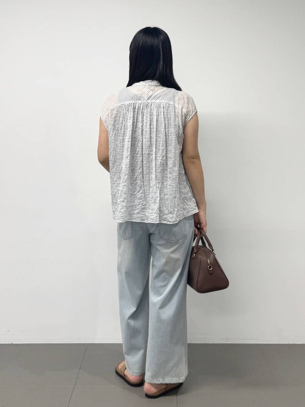ブラウン系のボストンバッグ、ブルー系のデニムパンツ、ブラウン系のサンダルを着用したレディースの夏コーディネートの3枚目の写真
