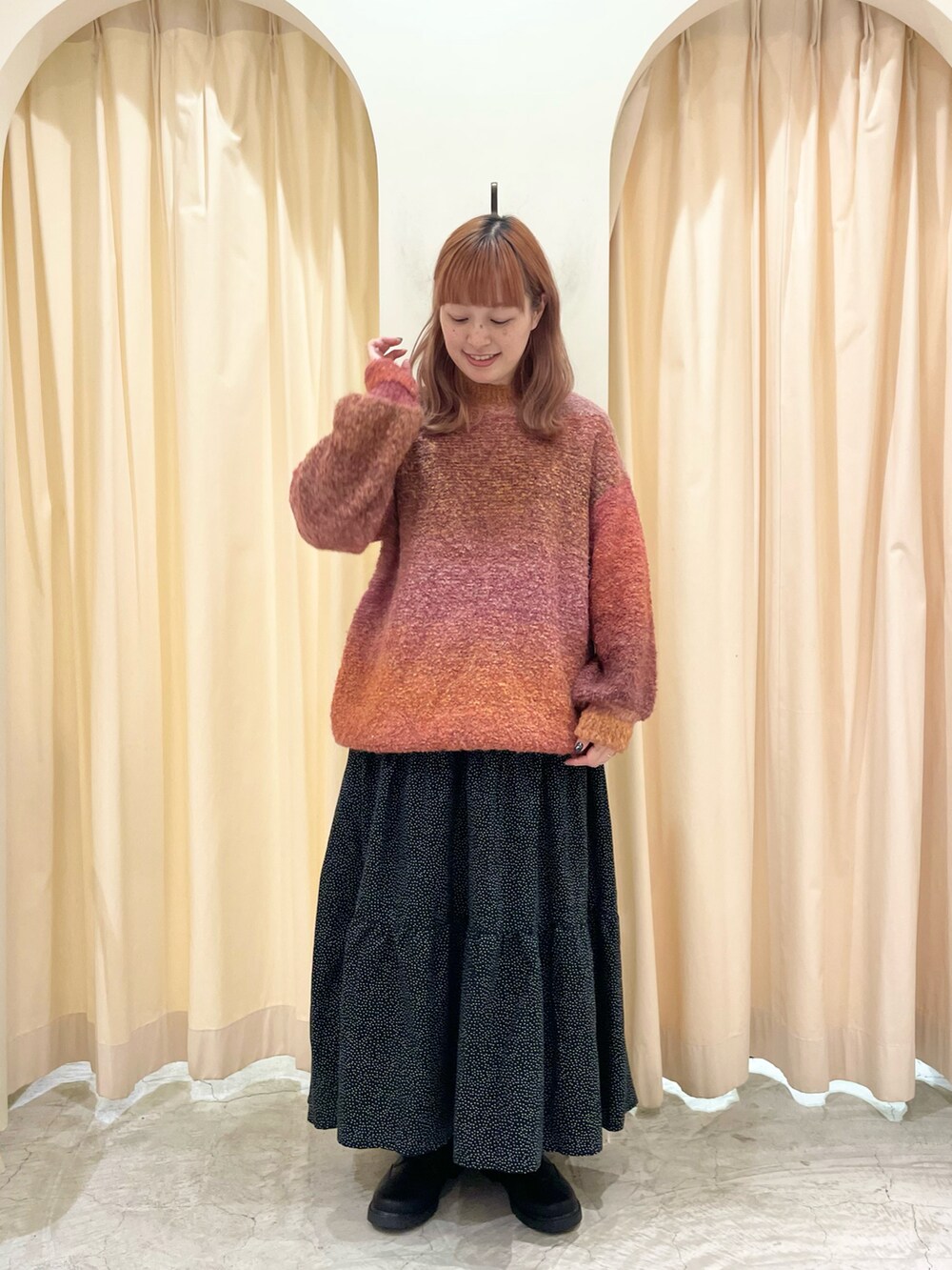 オレンジ系のニット/セーター、ブラック系のスカート、ブラック系のブーツを着用したレディースの冬コーディネートの2枚目の写真