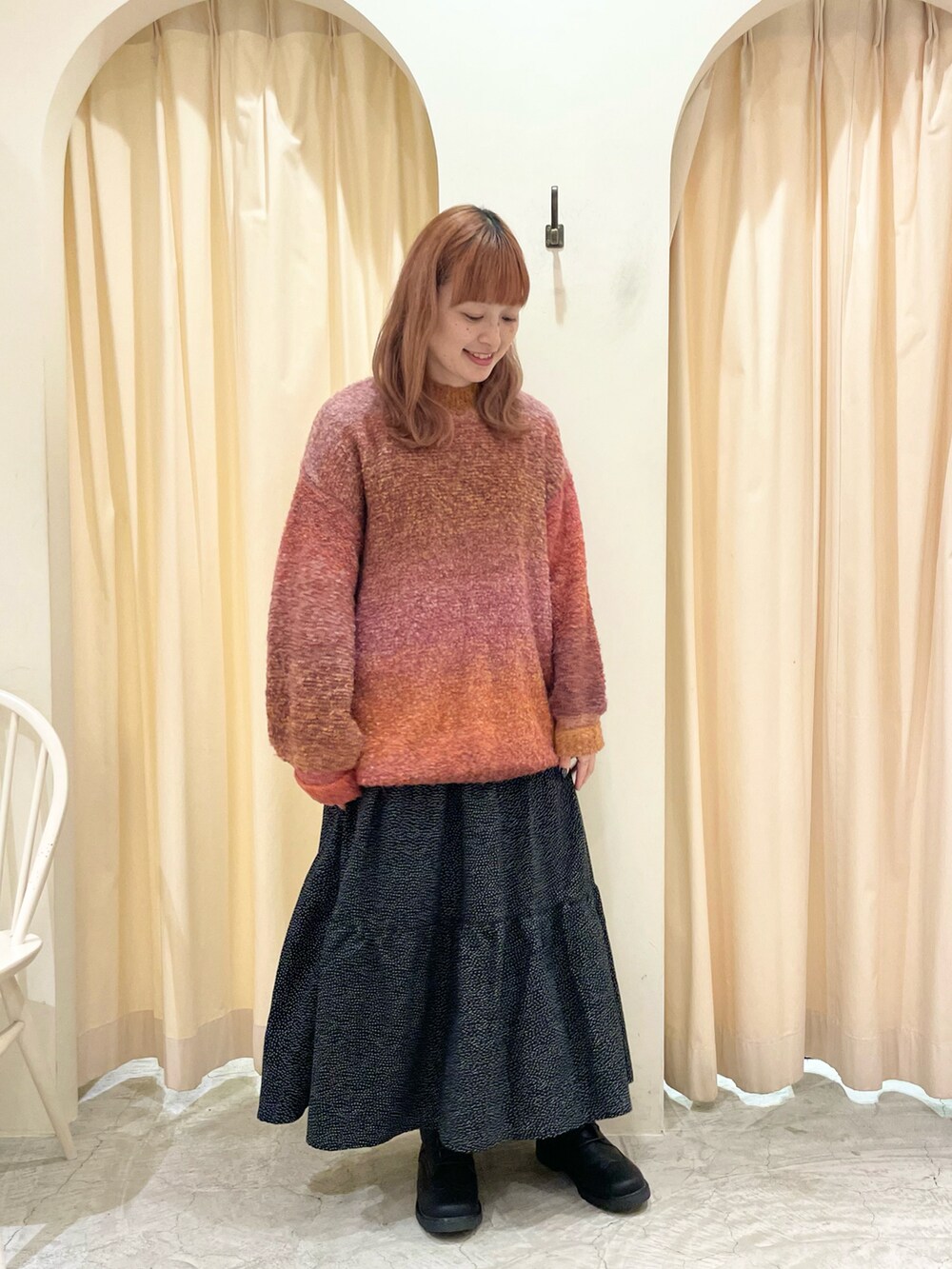 オレンジ系のニット/セーター、ブラック系のスカート、ブラック系のブーツを着用したレディースの冬コーディネートの3枚目の写真
