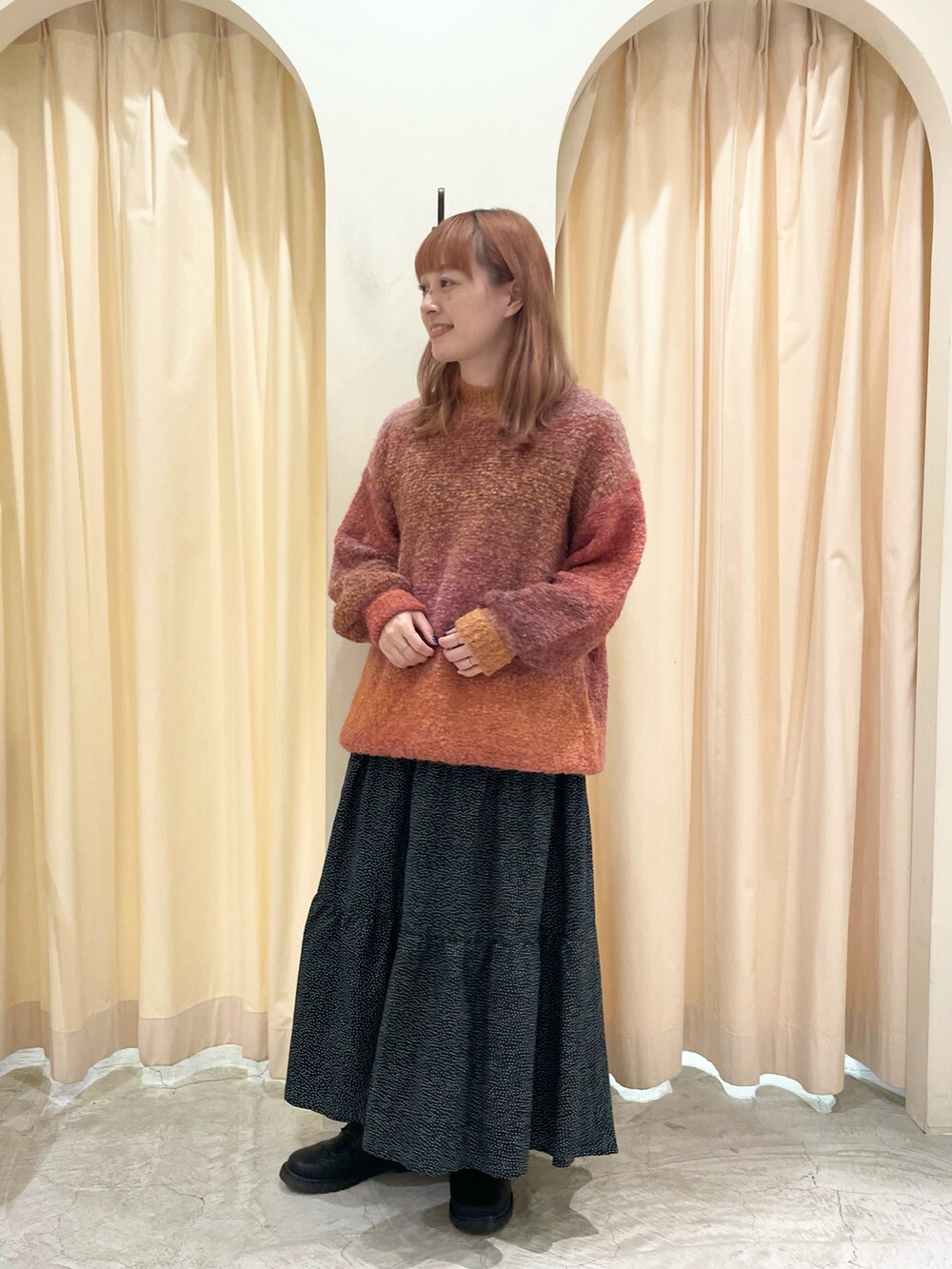 オレンジ系のニット/セーター、ブラック系のスカート、ブラック系のブーツを着用したレディースの冬コーディネートの4枚目の写真