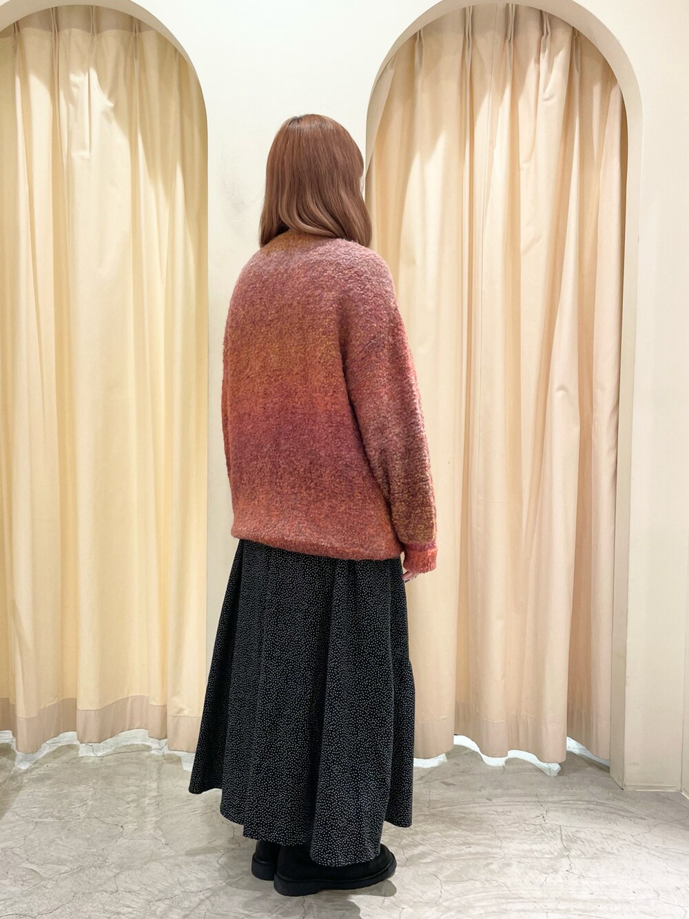 オレンジ系のニット/セーター、ブラック系のスカート、ブラック系のブーツを着用したレディースの冬コーディネートの5枚目の写真