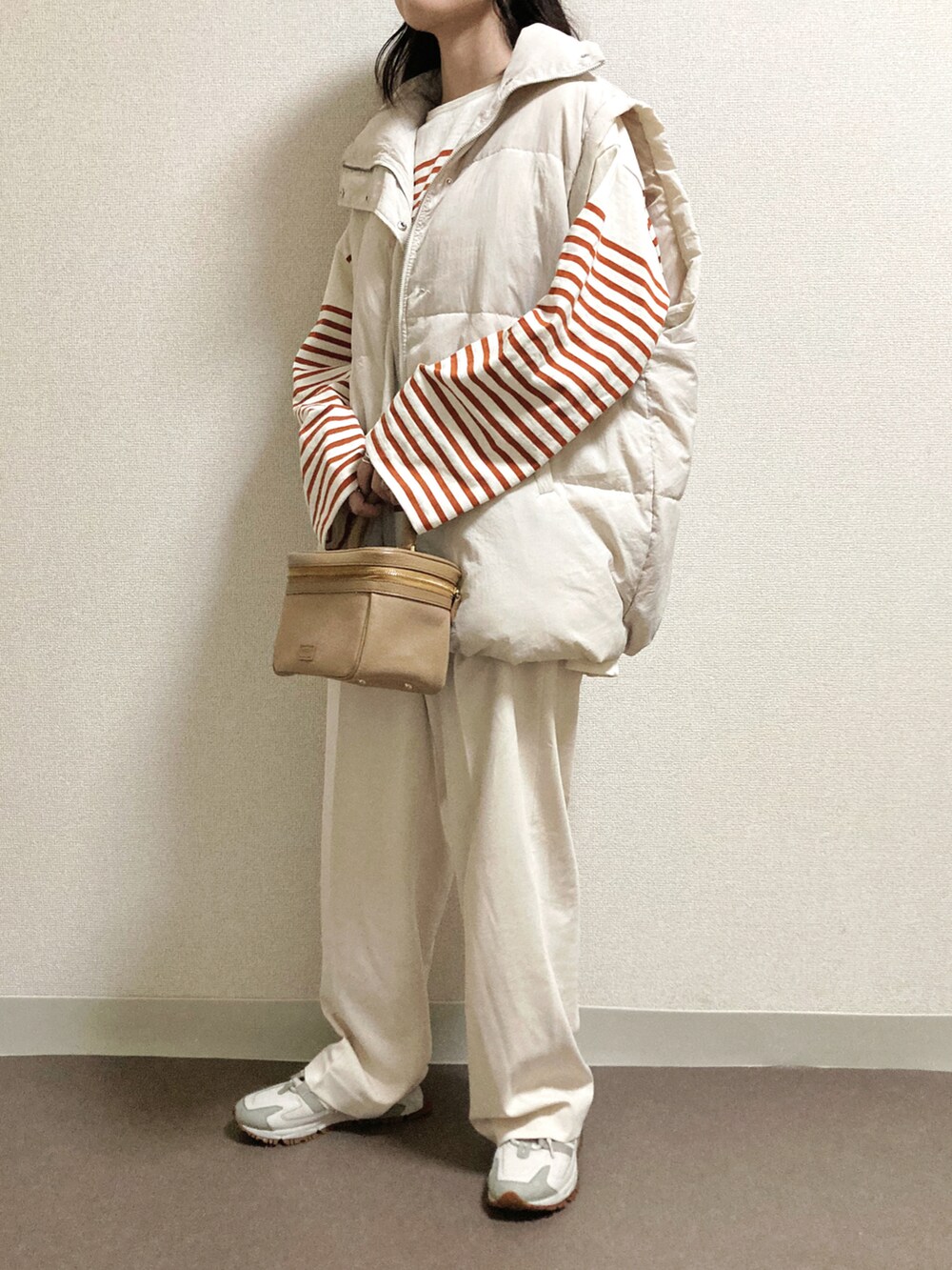 ホワイト系のスラックス、ホワイト系のダウンベスト、イエロー系のTシャツ/カットソーを着用したレディースの秋コーディネートの2枚目の写真