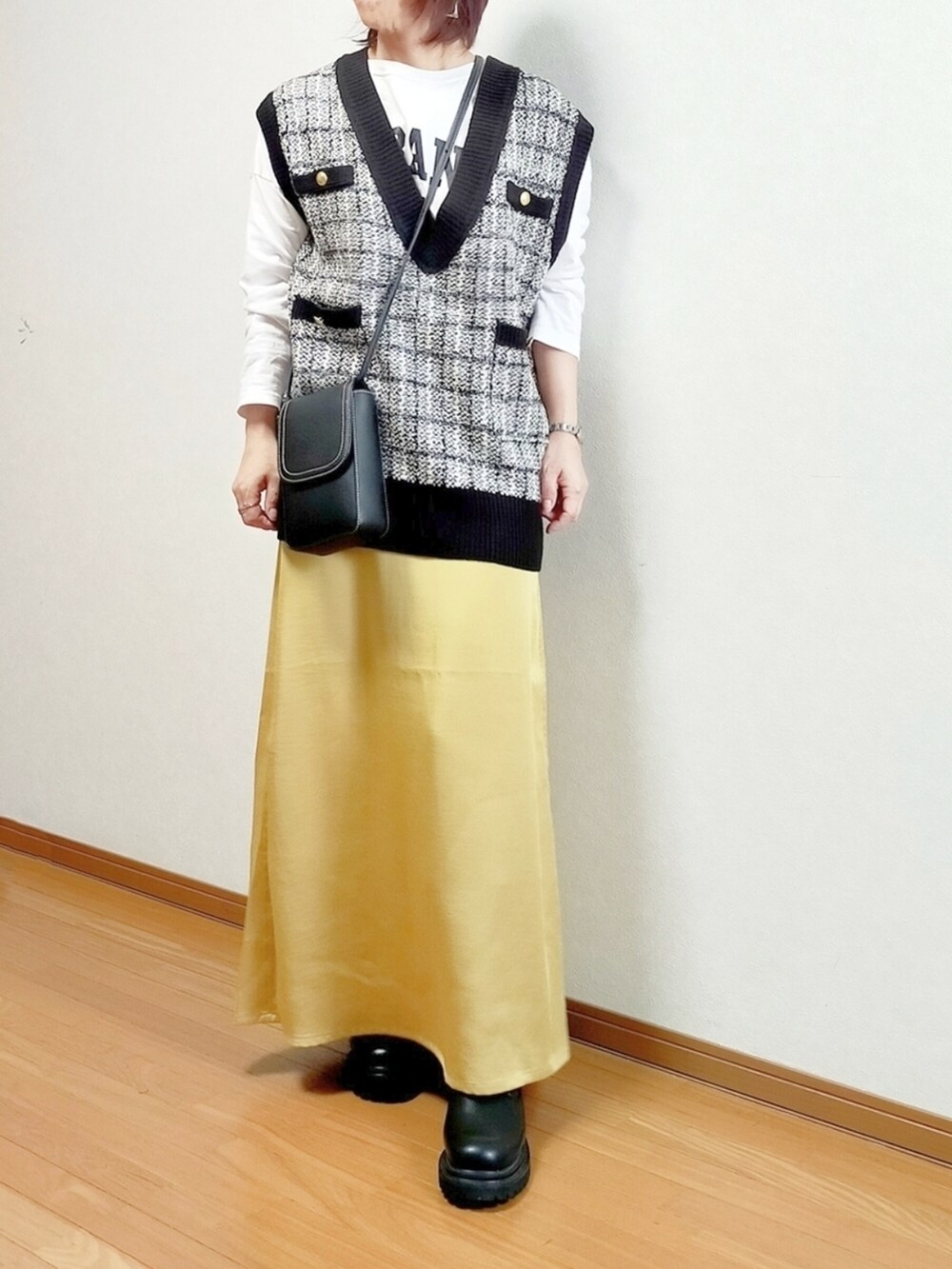 ブラック系のベスト、ホワイト系のTシャツ/カットソー、イエロー系のスカートを着用したレディースの秋コーディネートの2枚目の写真