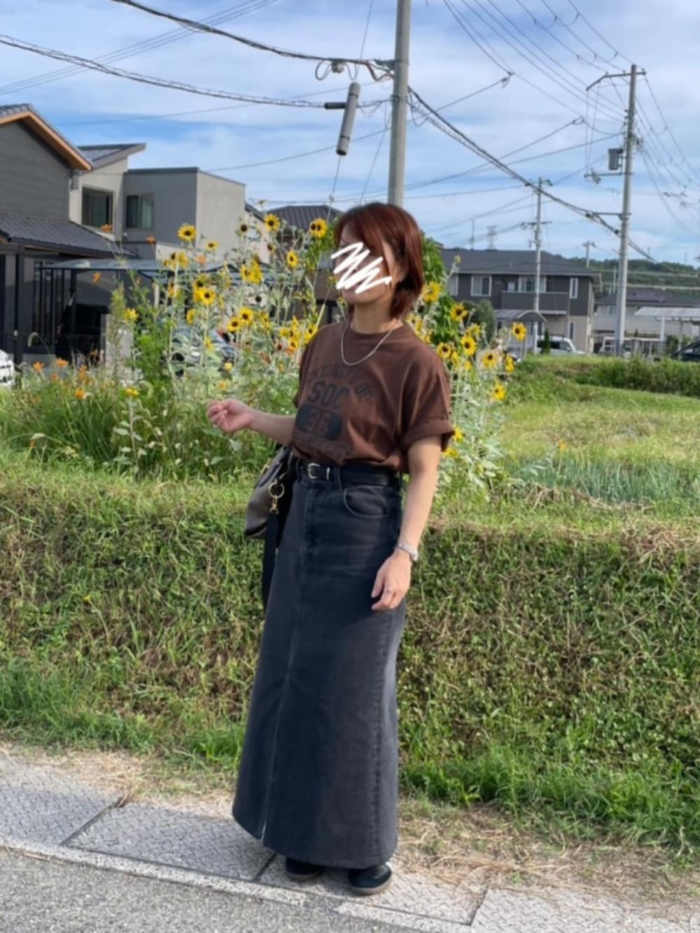 ブラウン系のTシャツ/カットソー、ブラック系のデニムスカート、ブラック系のスニーカーを着用したレディースの秋コーディネートの2枚目の写真