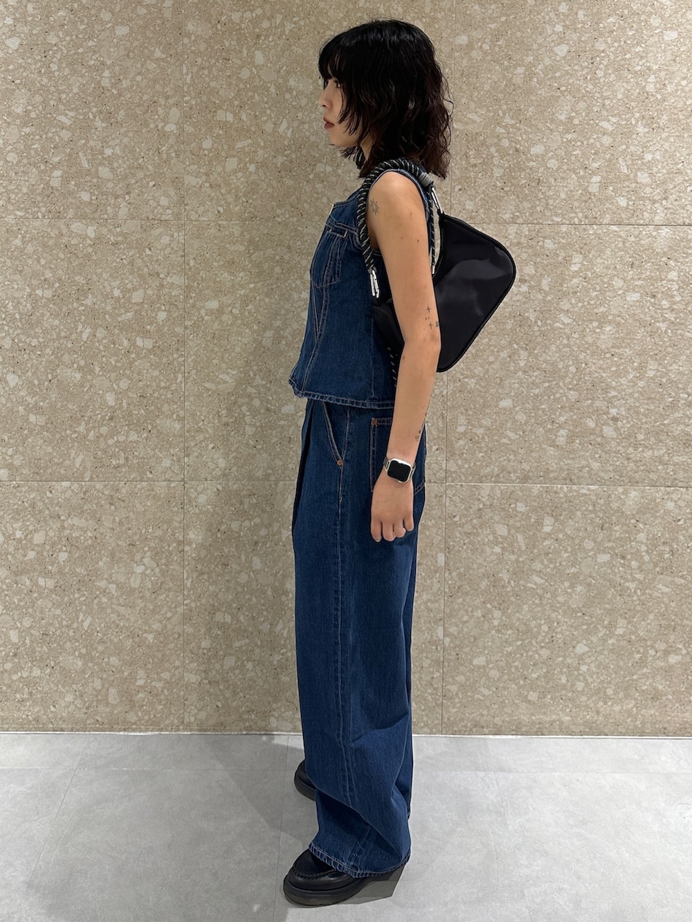 ブルー系のデニムパンツ、ブルー系のベスト、ブラック系のショルダーバッグを着用したレディースの夏コーディネートの3枚目の写真