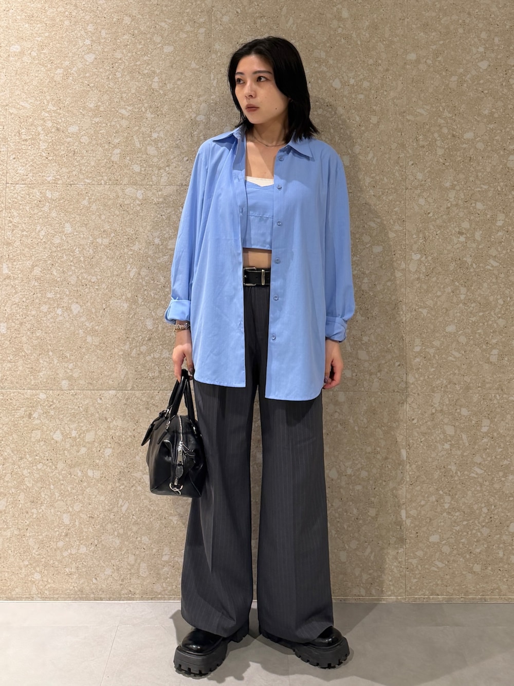 ブルー系のアンサンブル、グレー系のスラックス、ブラック系のショルダーバッグを着用したレディースの春コーディネートの2枚目の写真