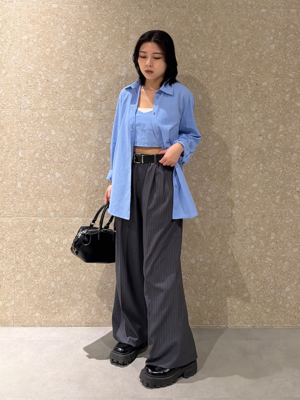 ブルー系のアンサンブル、グレー系のスラックス、ブラック系のショルダーバッグを着用したレディースの春コーディネートの3枚目の写真