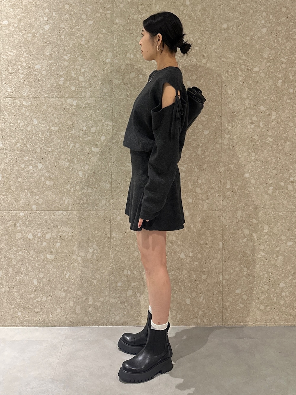 グレー系のワンピース、ブラック系のブーツ、ブラック系のショルダーバッグを着用したレディースの秋コーディネートの2枚目の写真