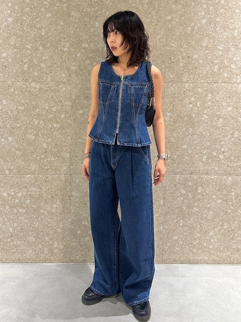 ブルー系のデニムパンツ、ブルー系のベスト、ブラック系のショルダーバッグを着用したレディースの夏コーディネートの2枚目の写真