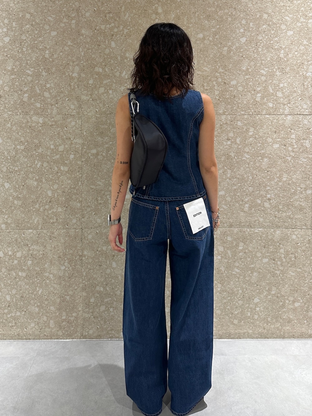 ブルー系のデニムパンツ、ブルー系のベスト、ブラック系のショルダーバッグを着用したレディースの夏コーディネートの4枚目の写真