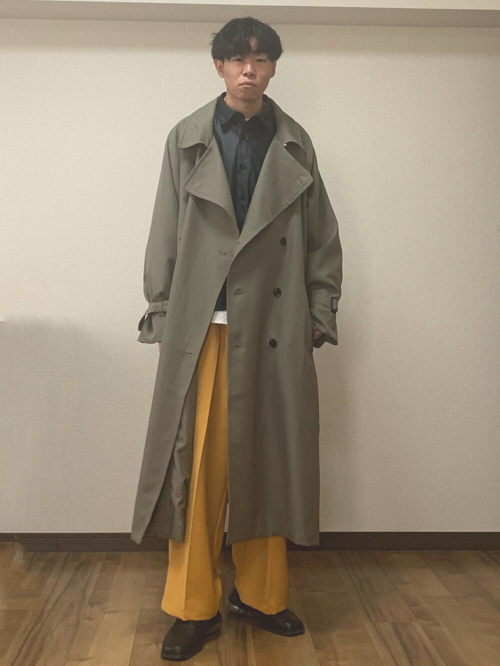 ベージュ系のトレンチコート、イエロー系のスラックス、ブラック系のローファーを着用したメンズの春コーディネートの2枚目の写真